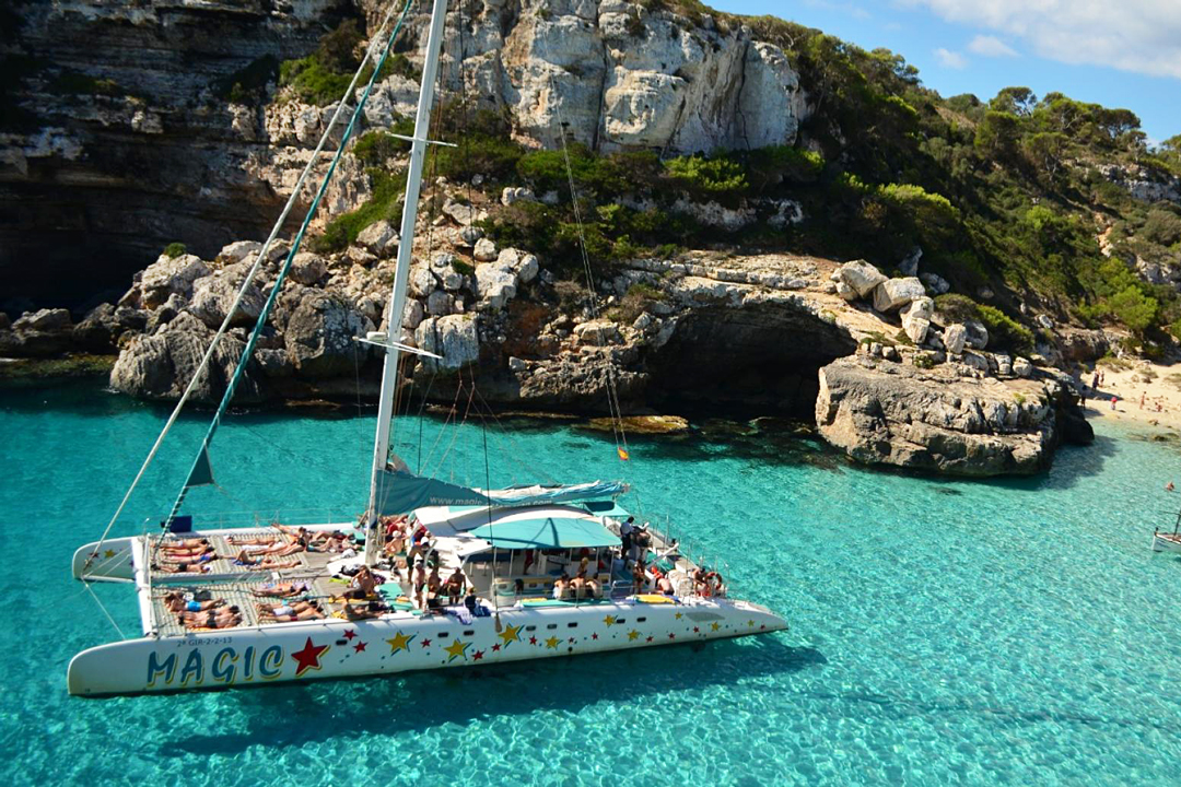Catamarán Magic navegando en aguas cristalinas de una cala de Mallorca