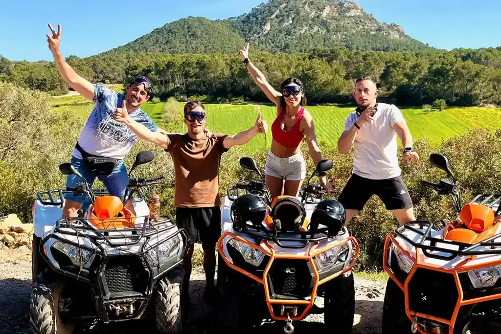 Eine Gruppe von Freunden steht mit drei bunten Quads vor einem grünen Hügel und einem Berg.
