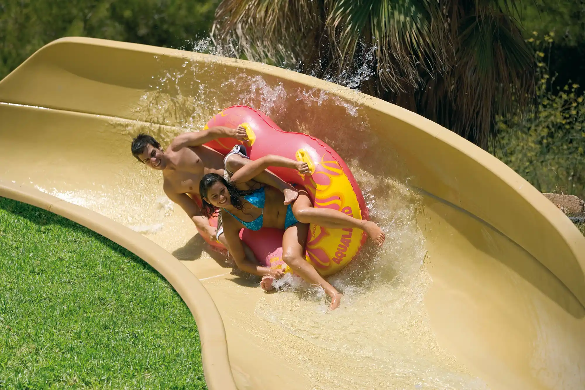 Young couple sliding down a water slide on an inflatable ring at a water park.