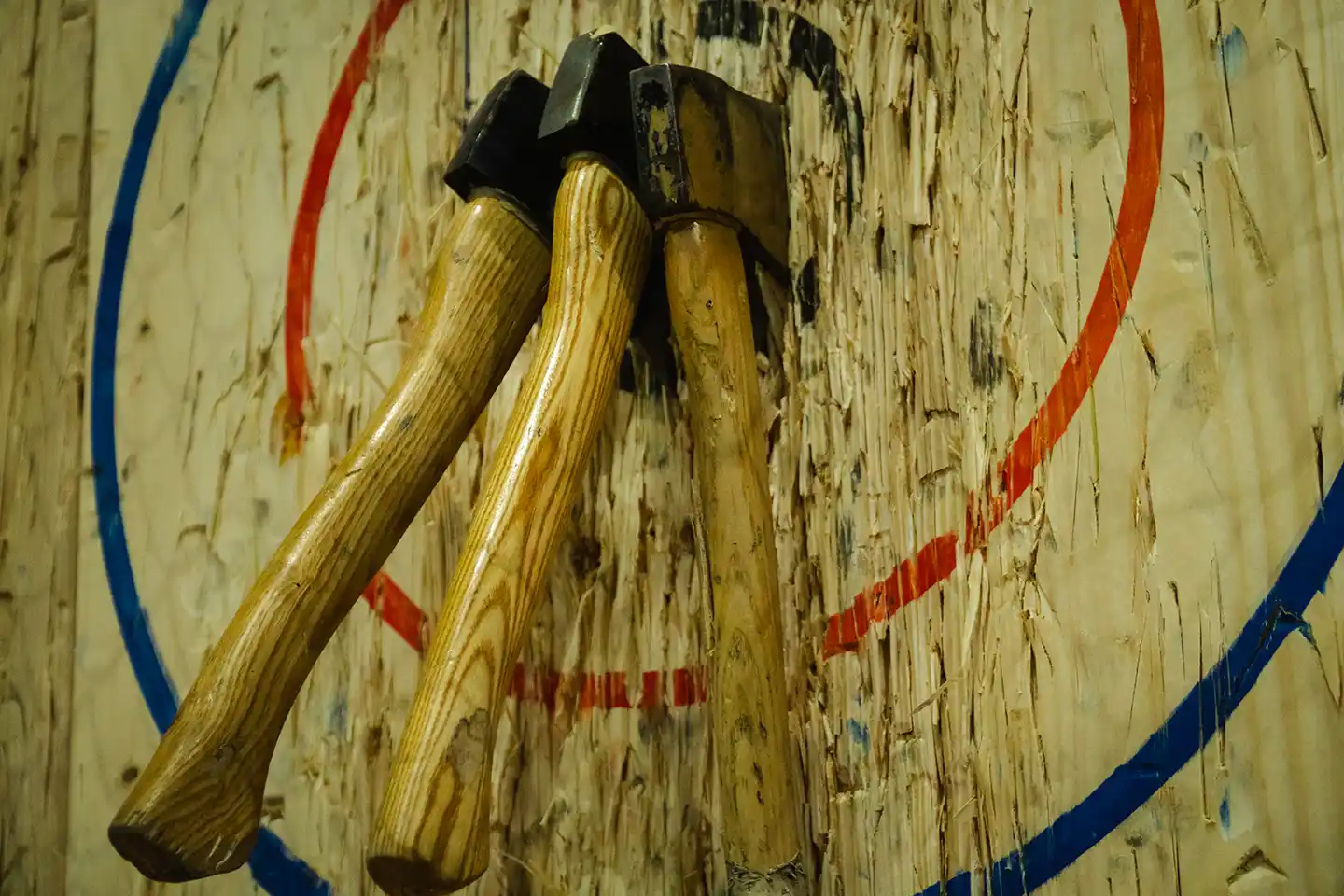 Three wooden axes embedded close together in the center of a worn target with blue and red circles.