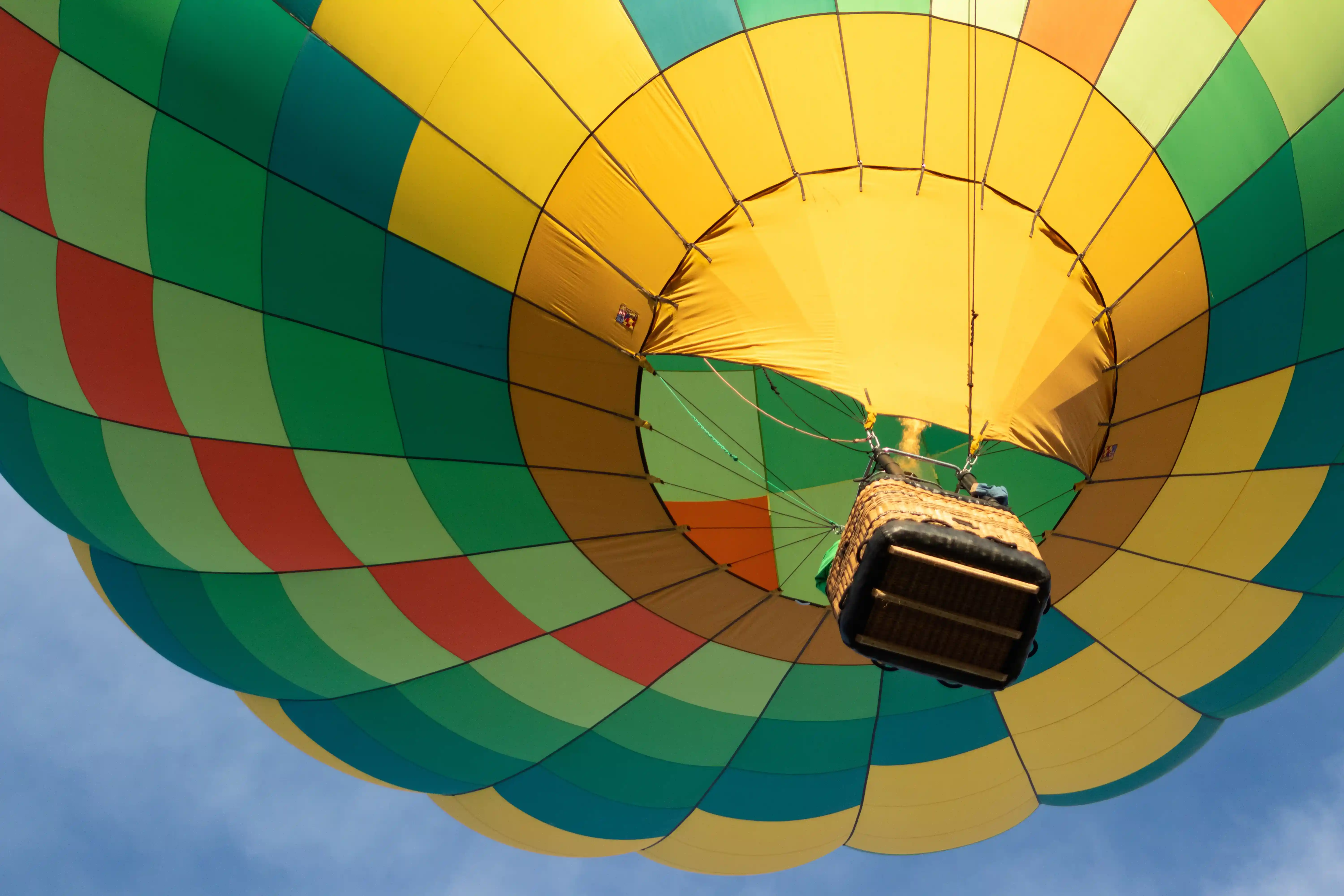 A low-angle view of a colorful hot air balloon with a wicker basket flying in the blue sky.