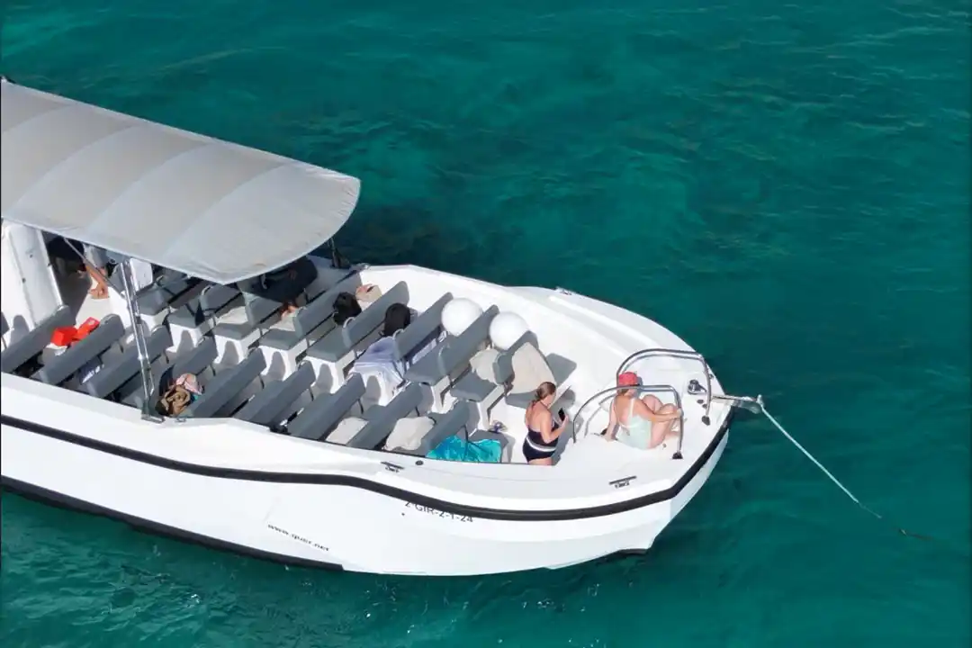 An overhead view of a white tourist boat with empty gray seats floating on clear turquoise sea water.