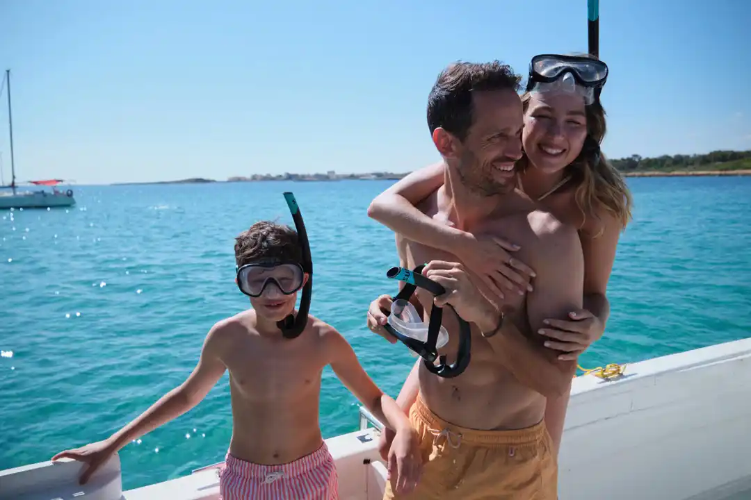 Eine glückliche Familie mit Schnorchelausrüstung lächelt auf einem Boot im türkisfarbenen Meer. Eine glückliche Familie mit Schnorchelausrüstung lächelt auf einem Boot im türkisfarbenen Meer.