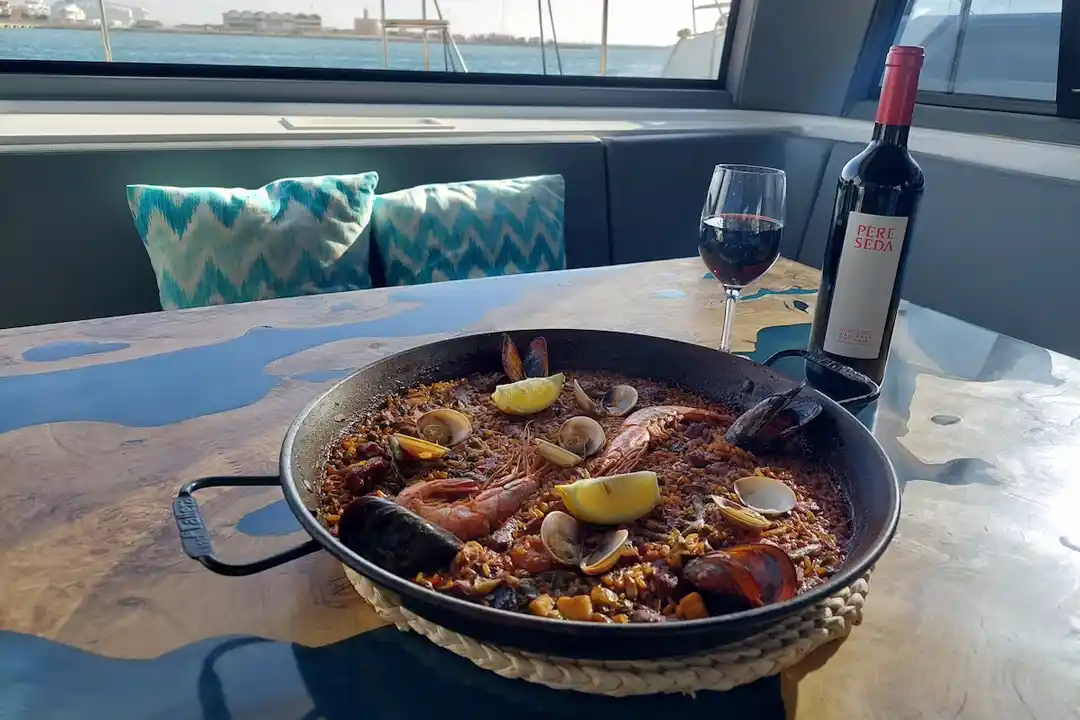 Une paella traditionnelle aux fruits de mer servie dans un plat sur la table d'un bateau avec du vin rouge. Une paella traditionnelle aux fruits de mer servie dans un plat sur la table d'un bateau avec du vin rouge.