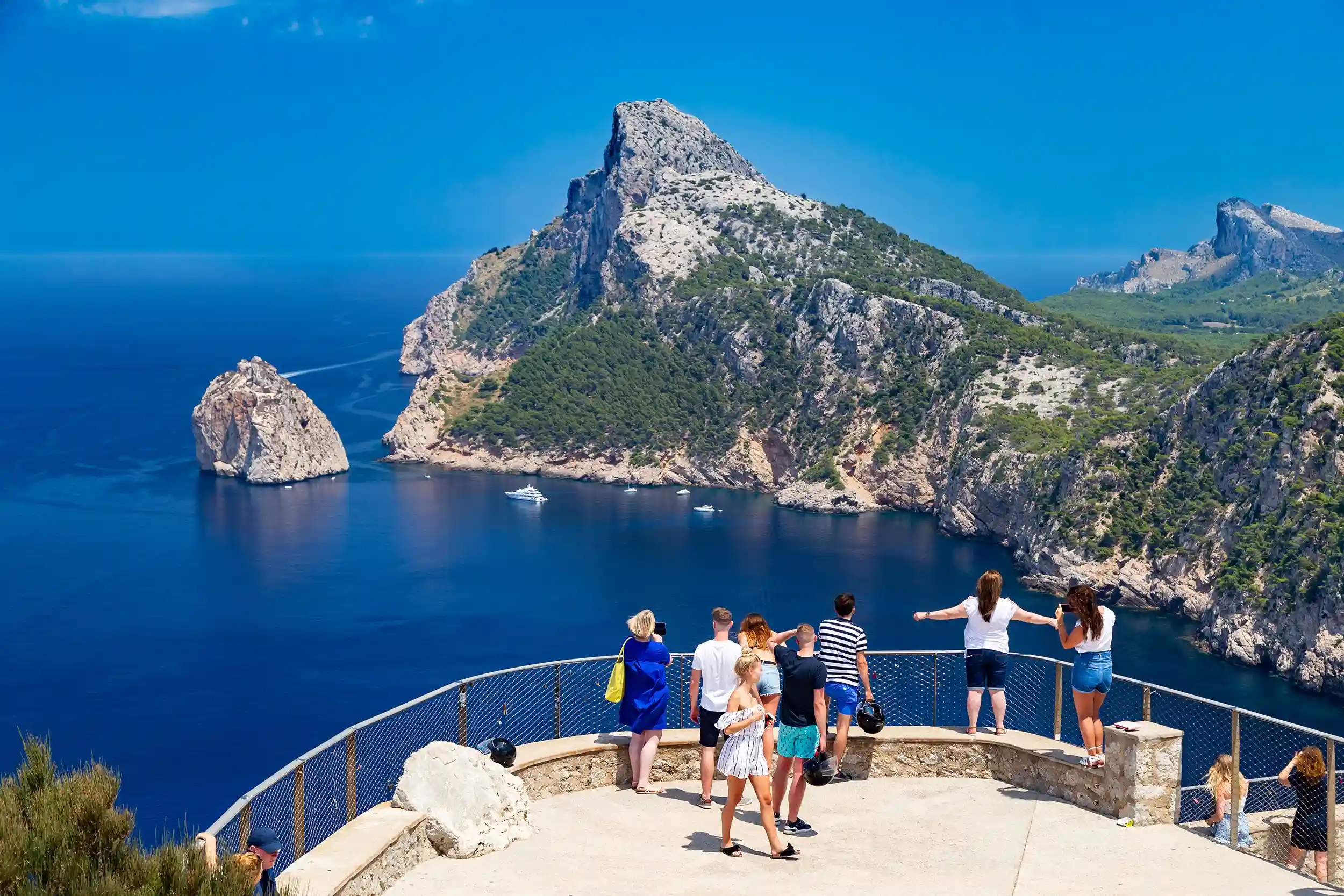 A group of tourists enjoying the scenic view of Cap de Formentor cliffs and the blue sea from a viewpoint in Mallorca.