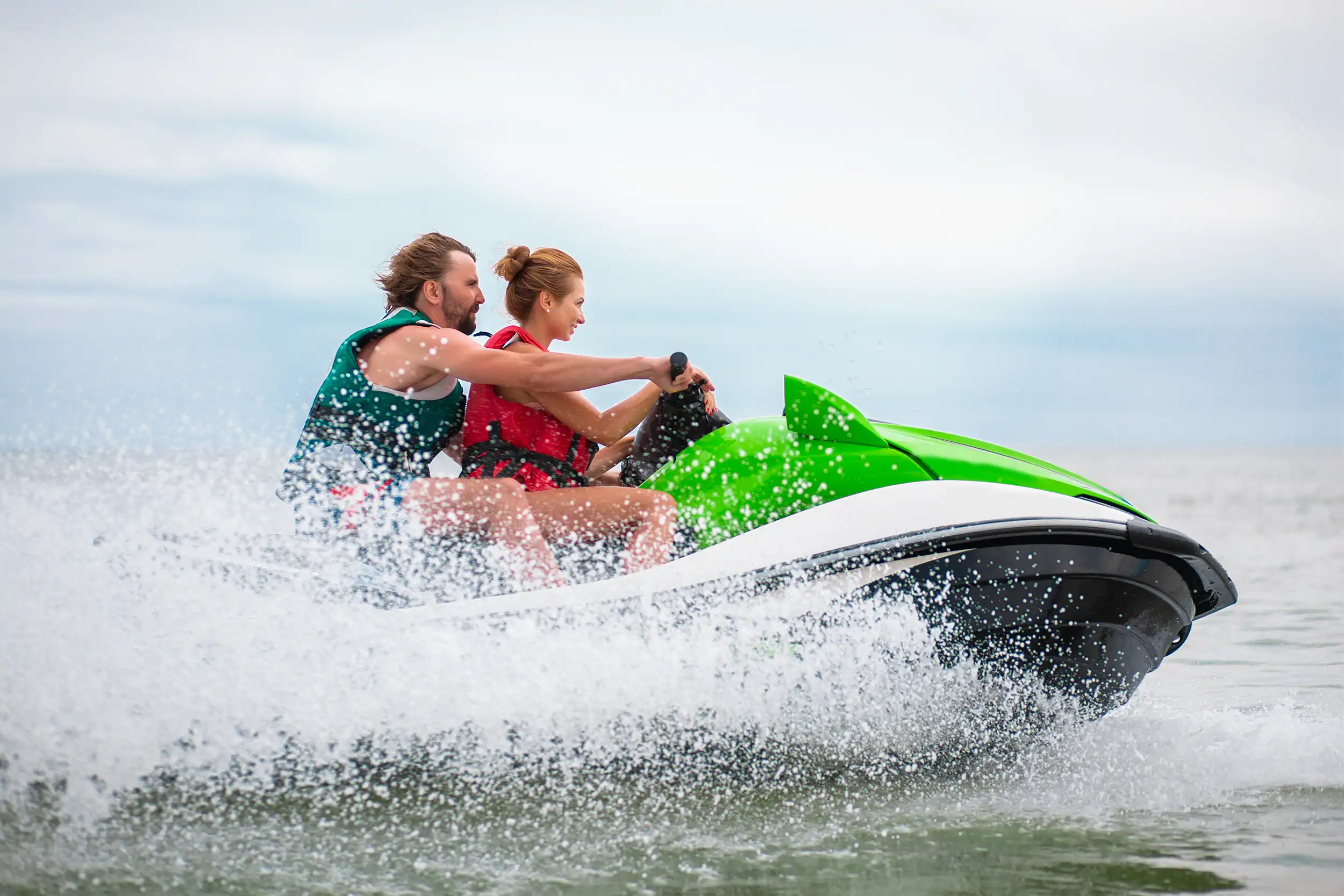 A man and a woman riding a green jet ski on the ocean creating big water splashes.