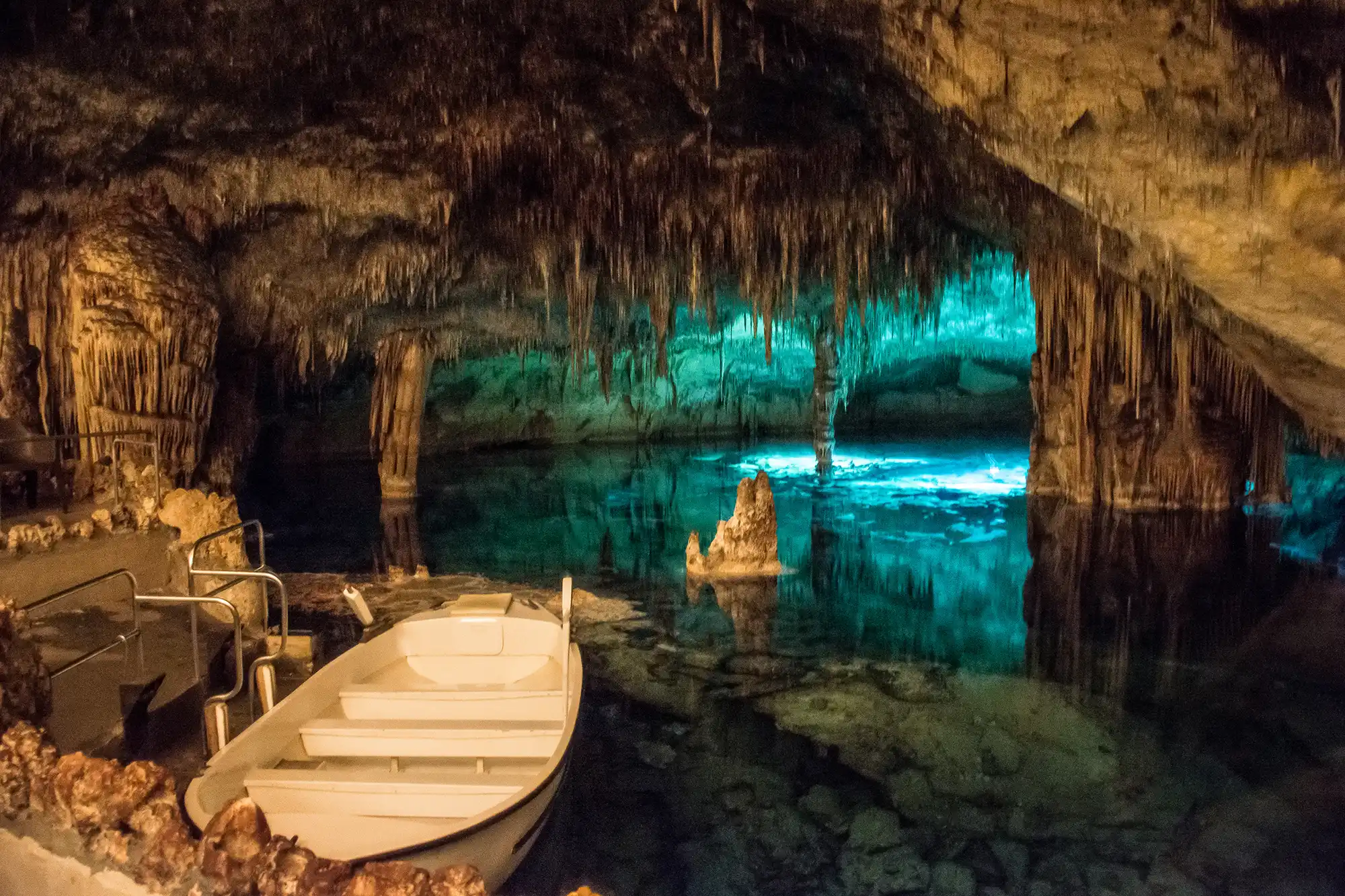 A white boat floating on a turquoise underground lake inside a cave with stalactites.
