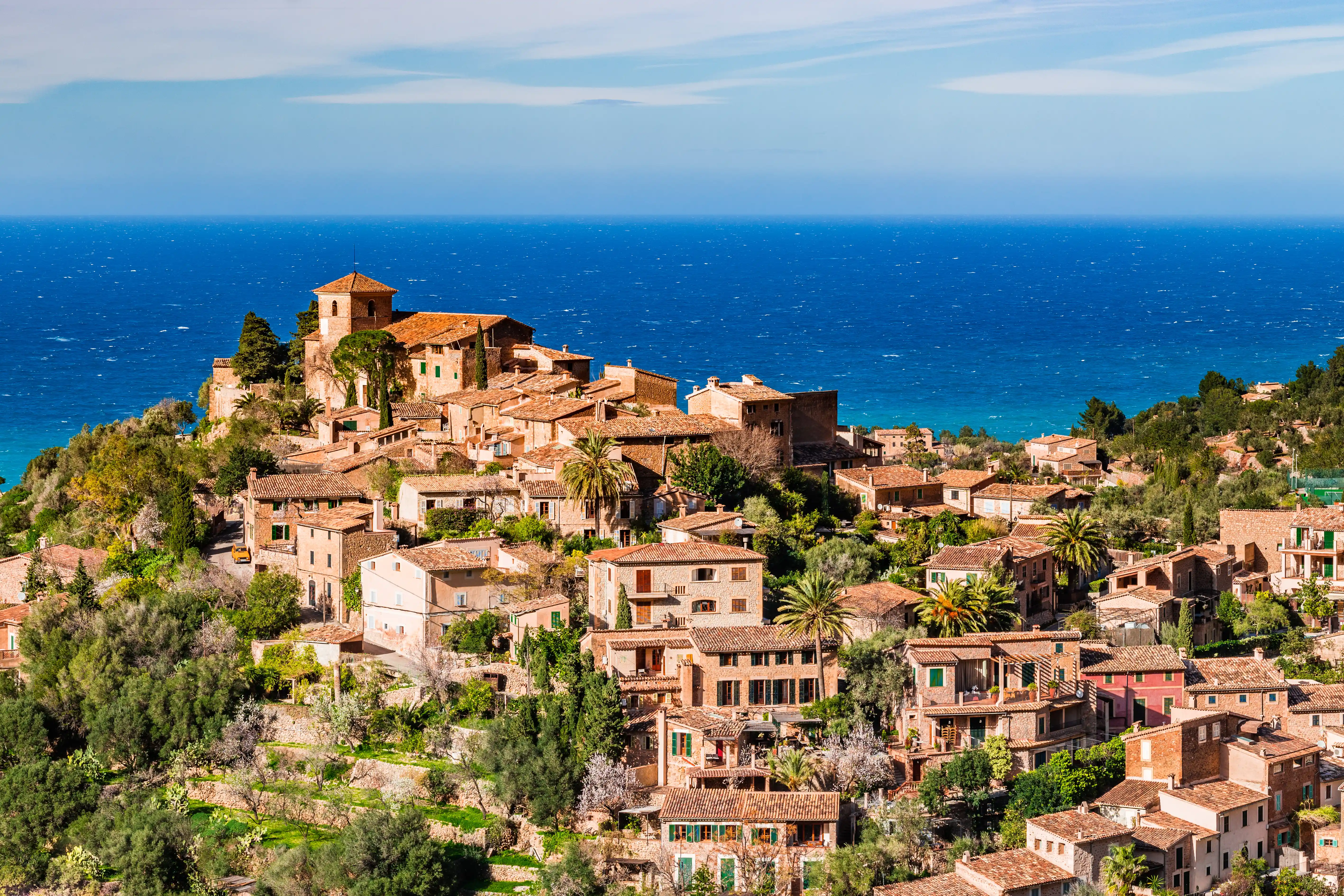 A scenic view of an old stone village on a green hill overlooking the deep blue Mediterranean Sea.