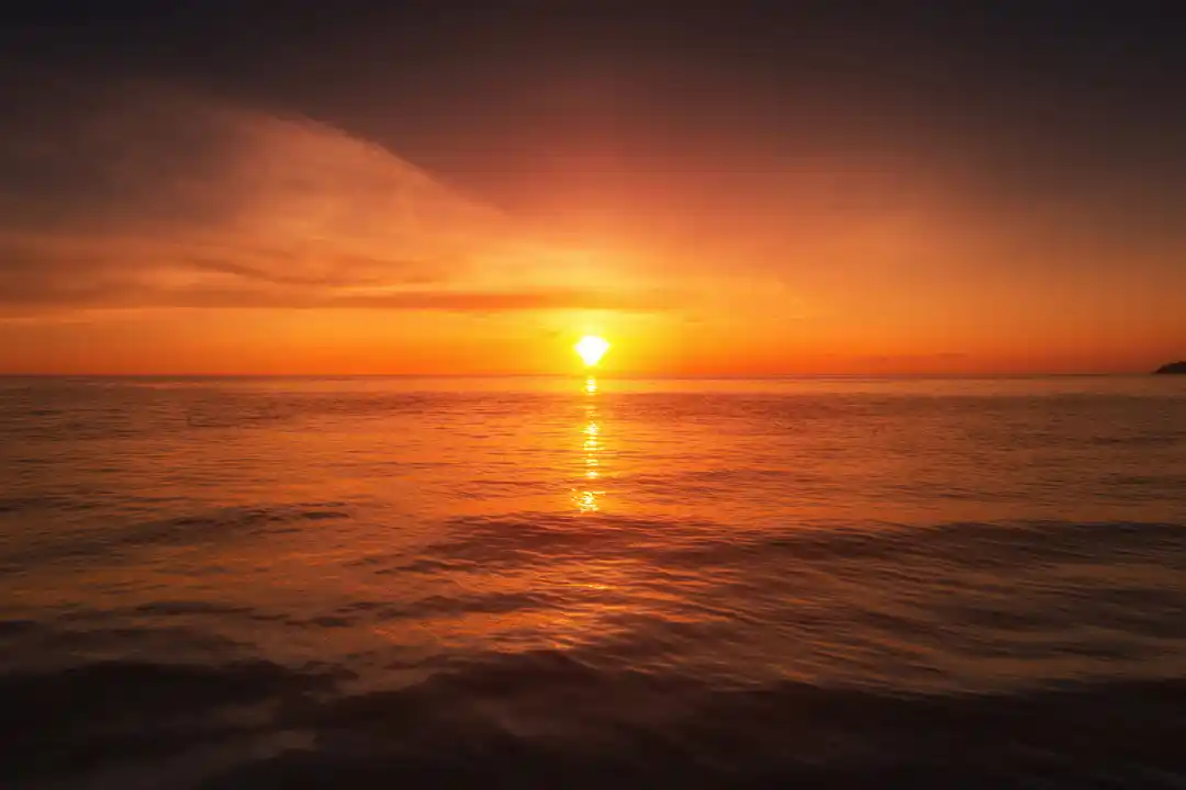 The sun sets over the calm sea, casting a vibrant golden and orange reflection across the water surface. The sun sets over the calm sea, casting a vibrant golden and orange reflection across the water surface.