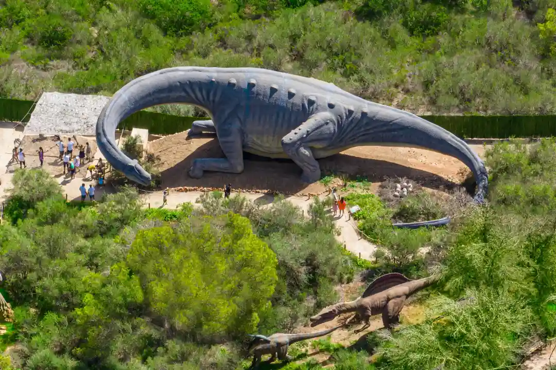 An aerial view of a huge dinosaur statue surrounded by lush green trees in a theme park.