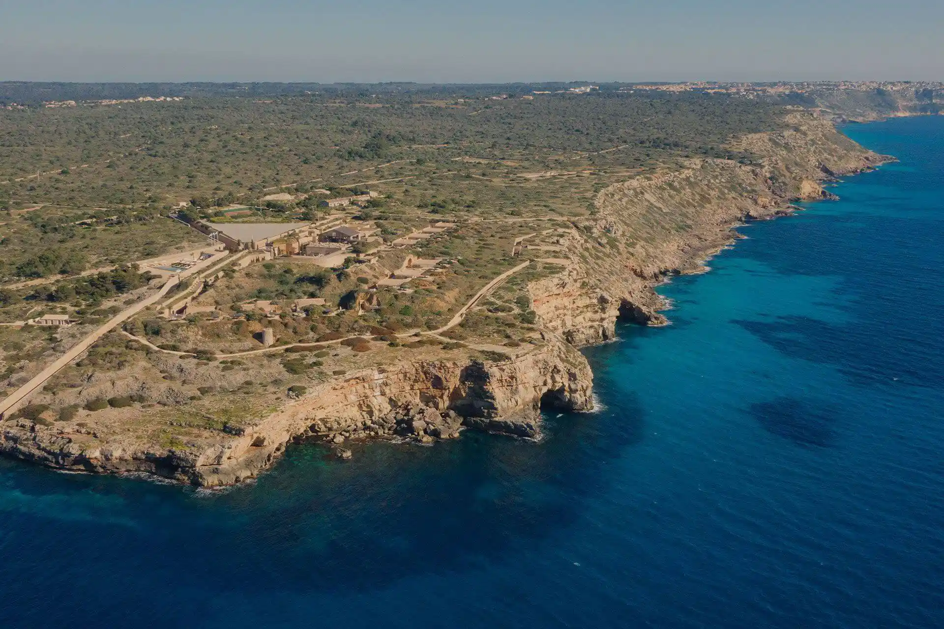 Eine Luftaufnahme einer felsigen Küste mit Klippen, die auf das klare türkisfarbene und blaue Meer treffen.