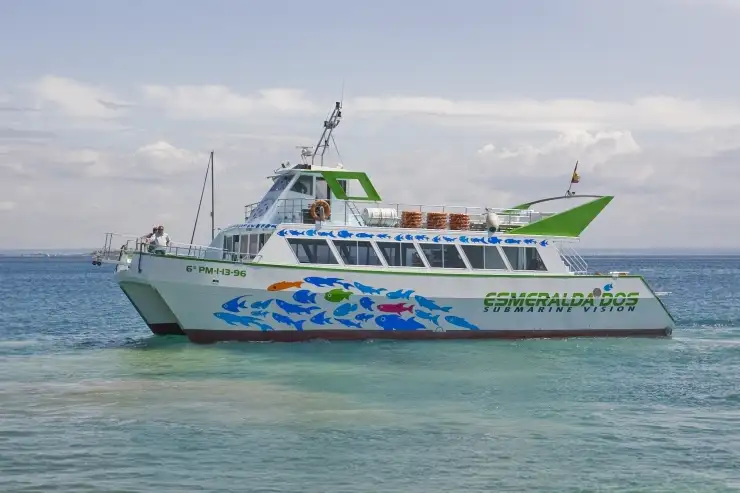 A white and green tourist ferry catamaran cruising on the calm blue sea under a cloudy sky.