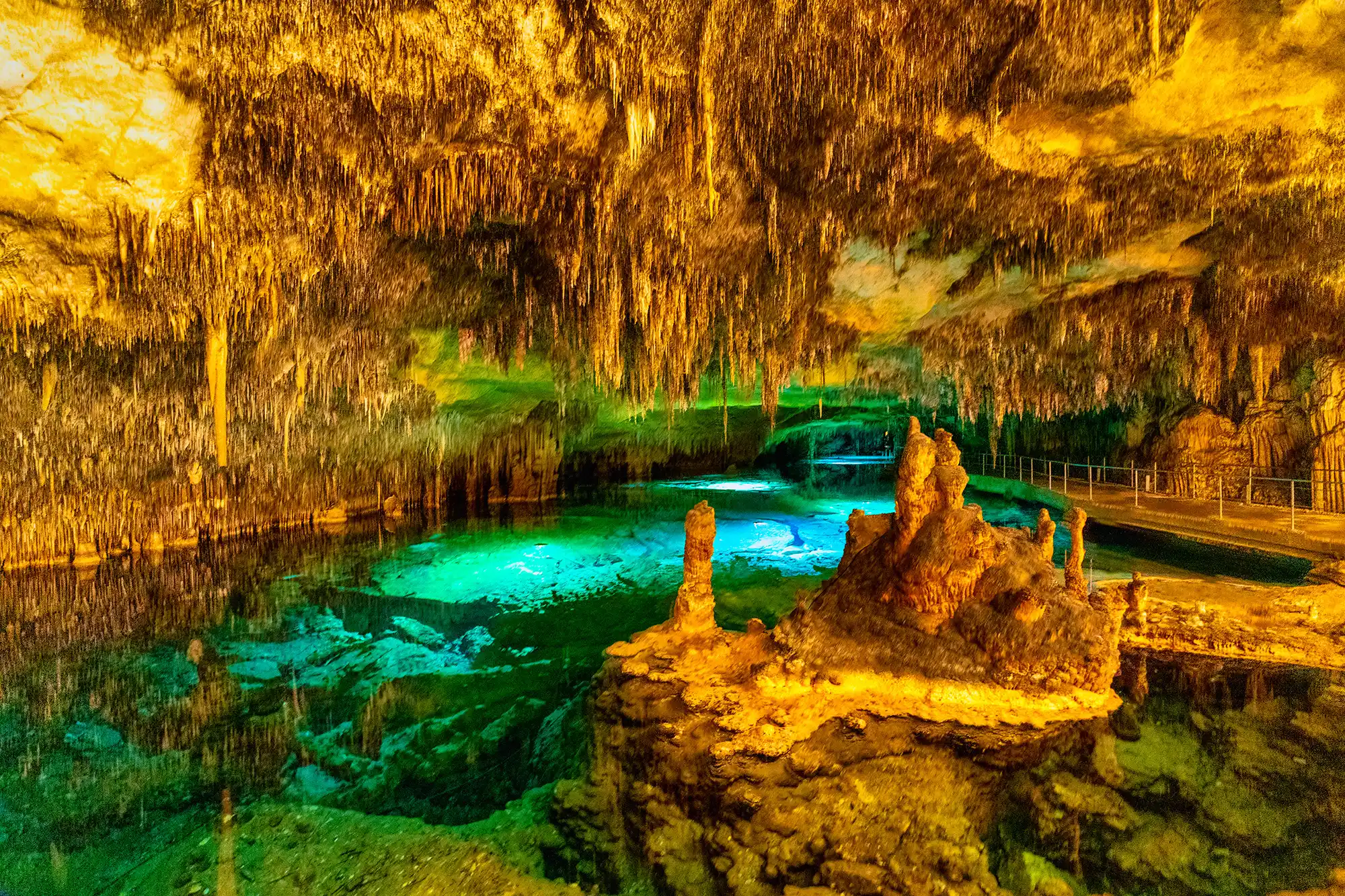 A beautiful turquoise underground lake illuminated inside a cave with stalactites and stalagmites.