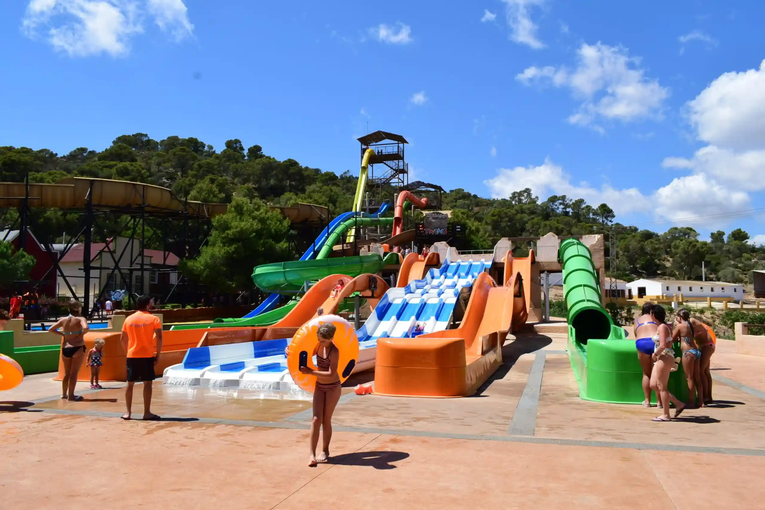 A variety of colorful water slides at a water park with people walking around on a sunny day.