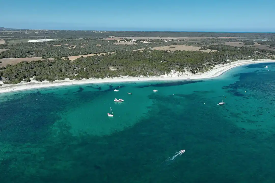 Eine Luftansicht von kleinen Booten, die nahe einem weißen Sandstrand mit grünen Bäumen im türkisfarbenen Wasser ankern.