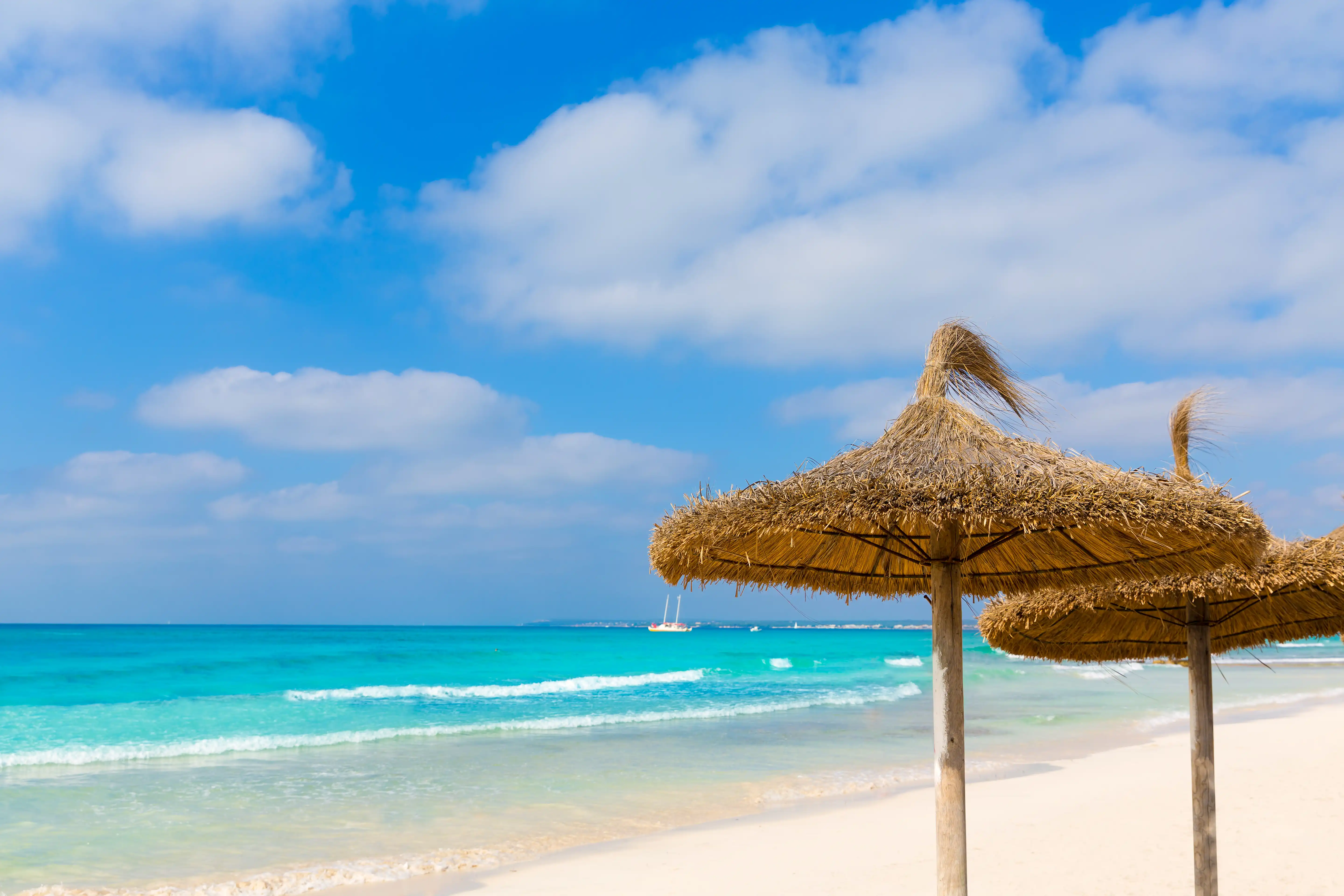 Straw umbrellas on the white sand of Es Trenc beach with turquoise water and blue sky.