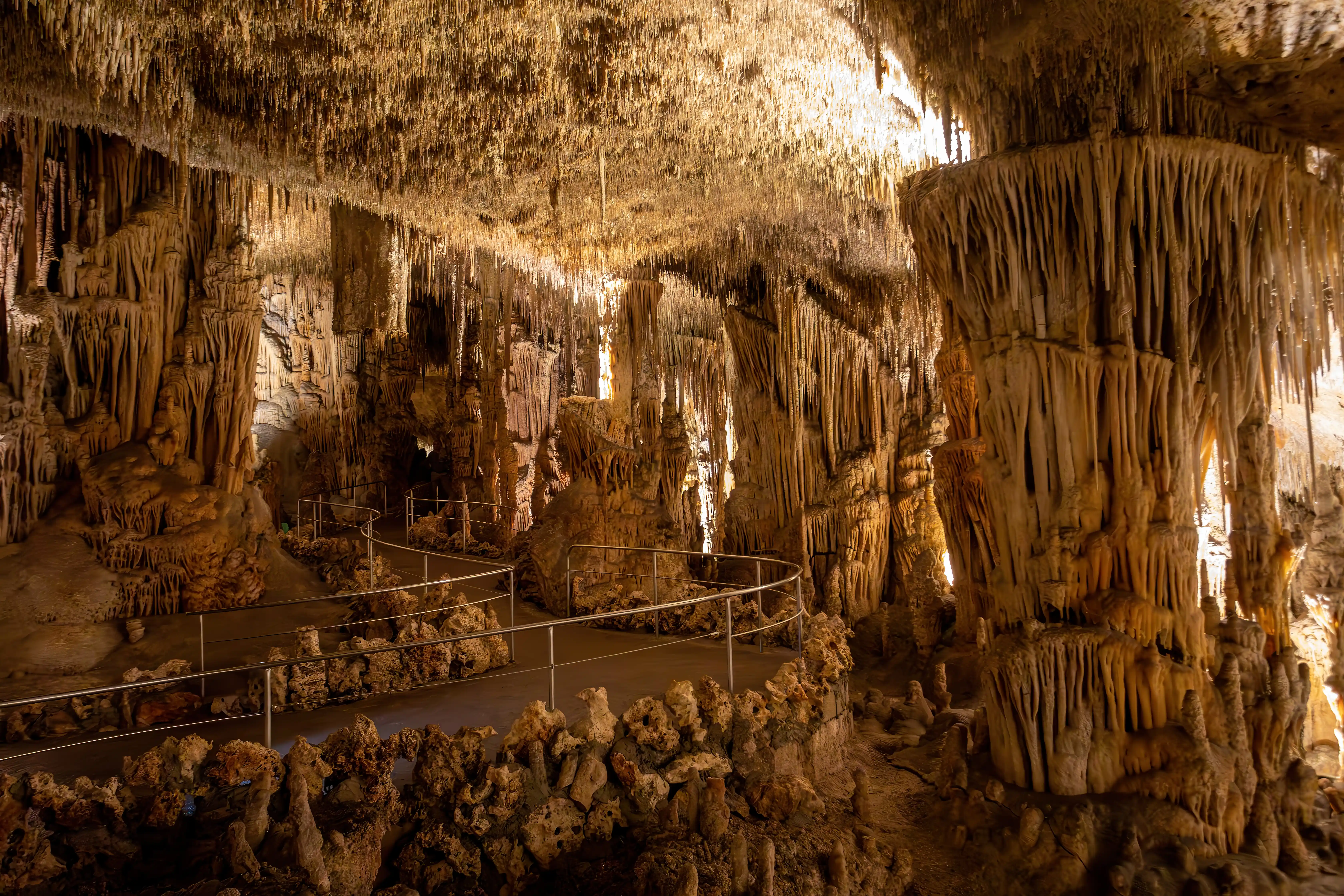 An impressive walkway winds through a massive underground rock cave filled with complex stalactites.