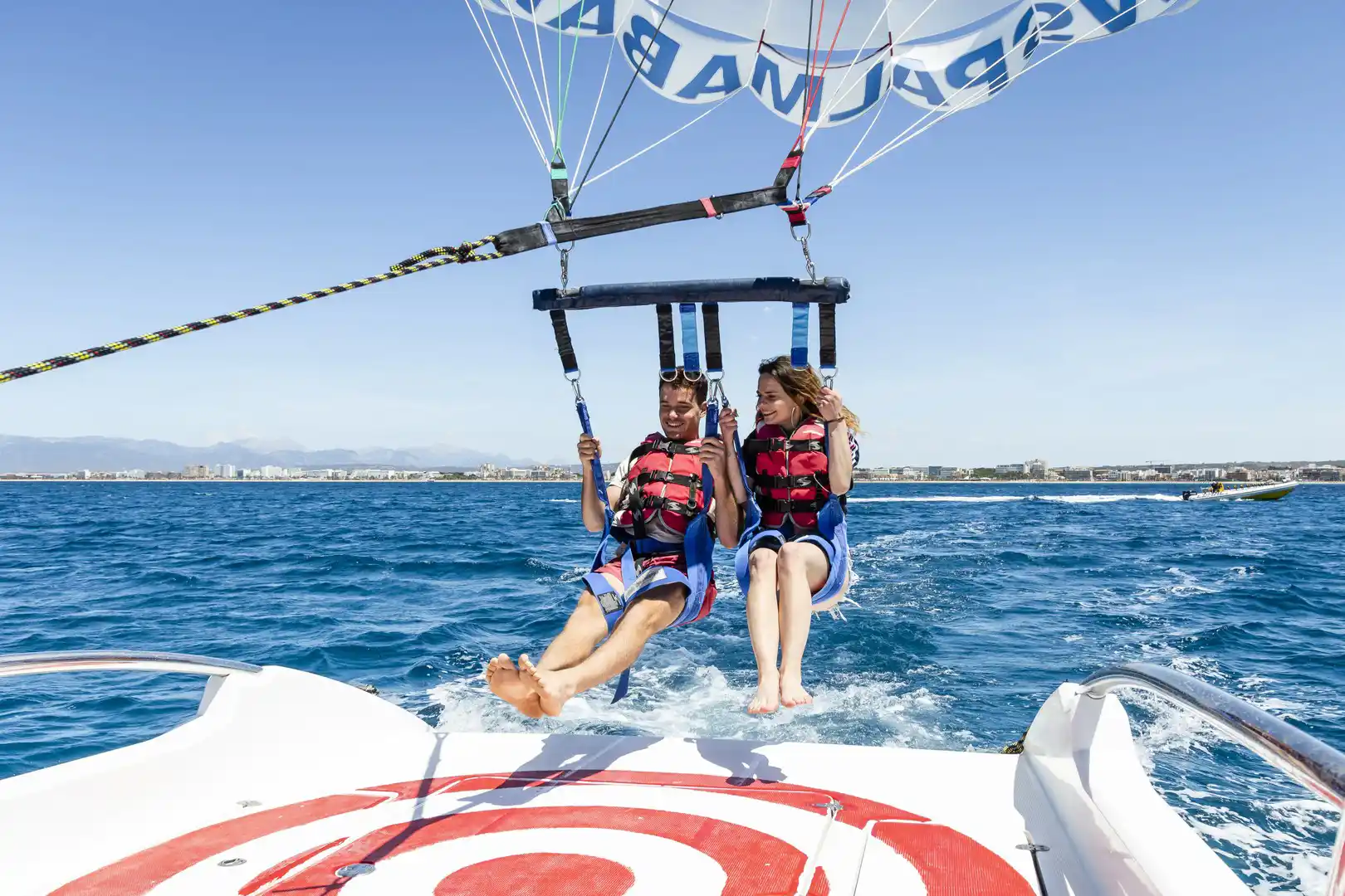 Zwei junge Menschen beim Parasailing direkt über dem Bootsdeck auf dem blauen Meerwasser. Zwei junge Menschen beim Parasailing direkt über dem Bootsdeck auf dem blauen Meerwasser.