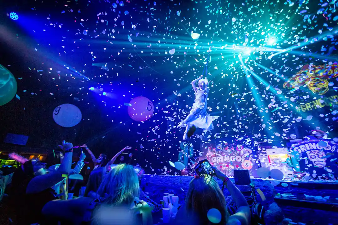 An performer dances on stage under falling confetti and bright laser lights during a lively nightclub party event.