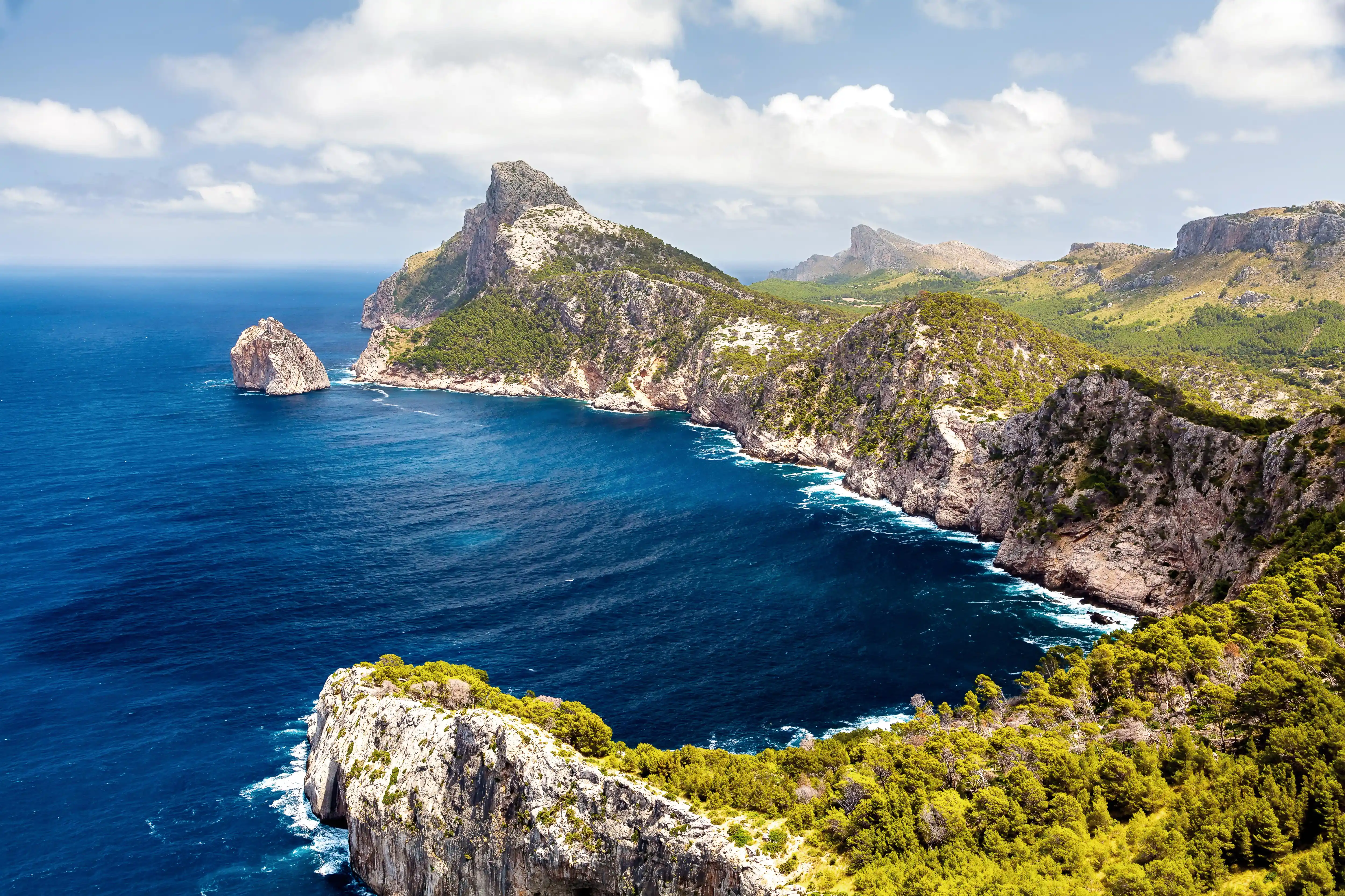 A breathtaking view of rocky cliffs and green mountains meeting the deep blue sea at Formentor in Mallorca.
