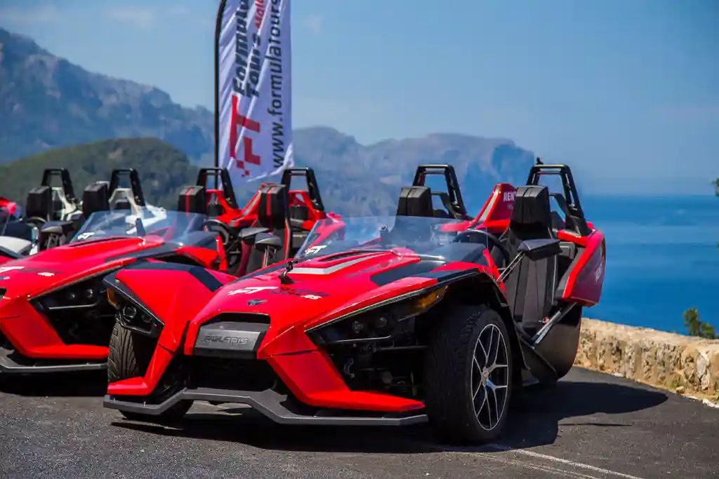 Red three-wheeled Slingshot cars parked on a coastal road overlooking the blue sea and mountains. Red three-wheeled Slingshot cars parked on a coastal road overlooking the blue sea and mountains.