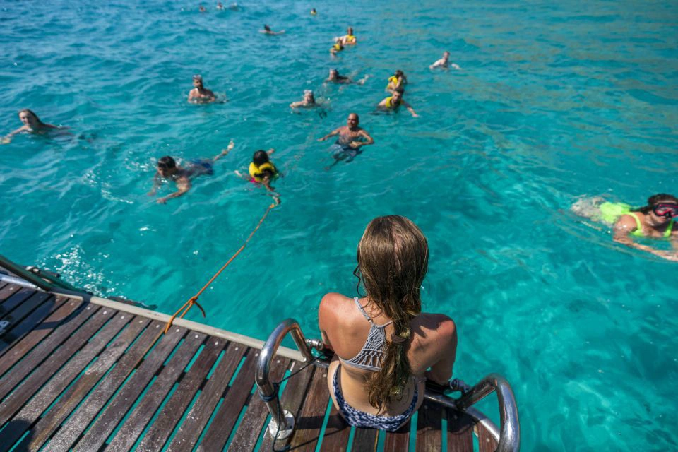 A woman sitting on a boat deck ladder watching people swimming in clear turquoise water. A woman sitting on a boat deck ladder watching people swimming in clear turquoise water.