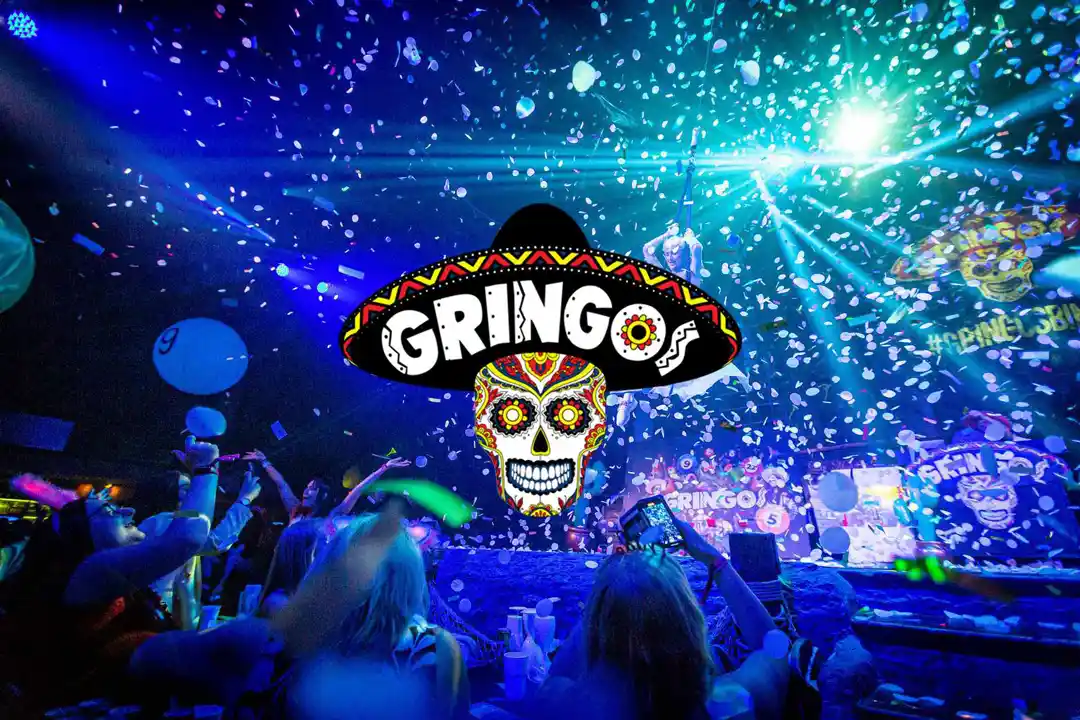 A party crowd under confetti and bright lights at a club, with a central Gringos logo featuring a skull with a sombrero.
