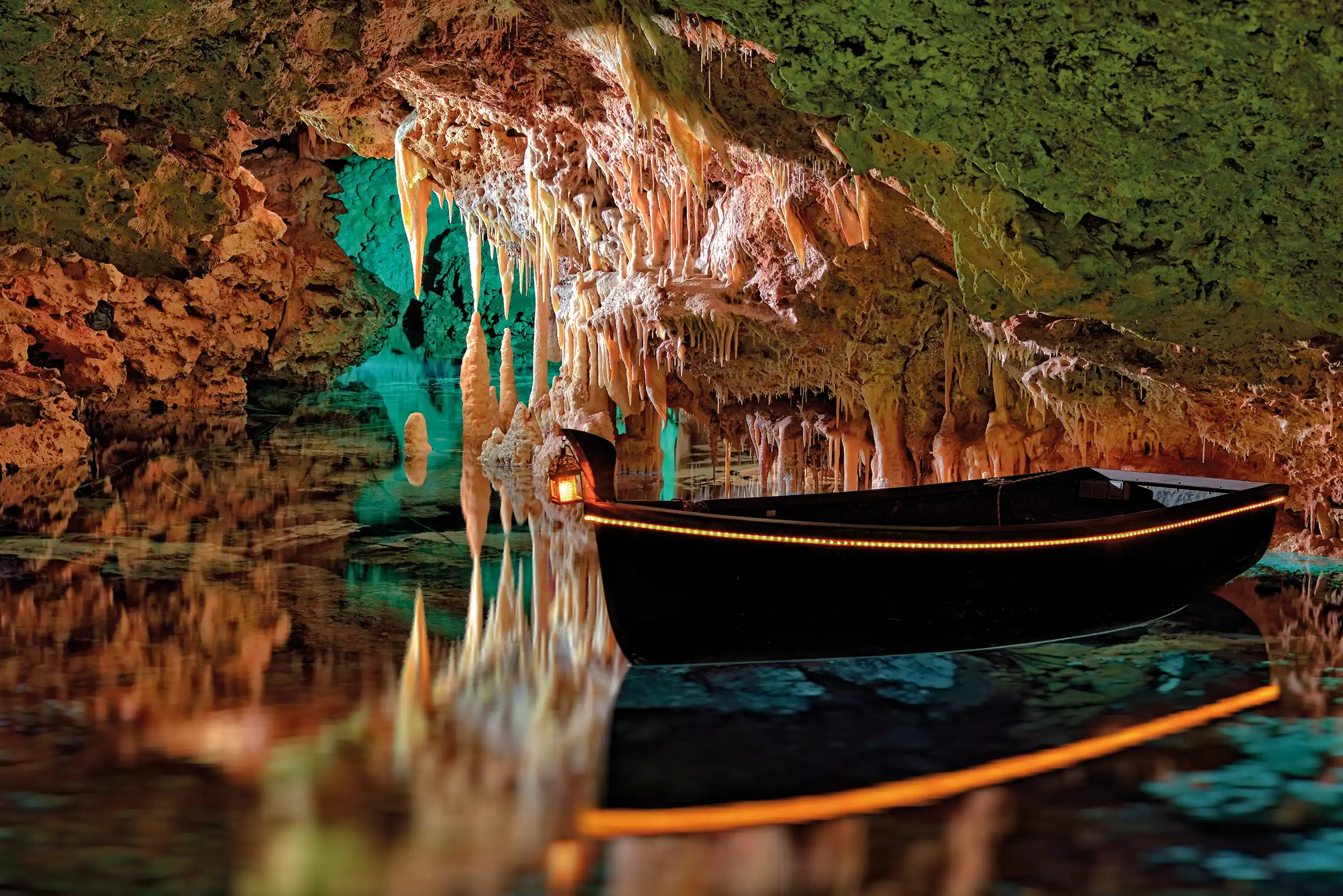 A small rowboat floating on a calm underground lake inside an illuminated cave with hanging stalactites.