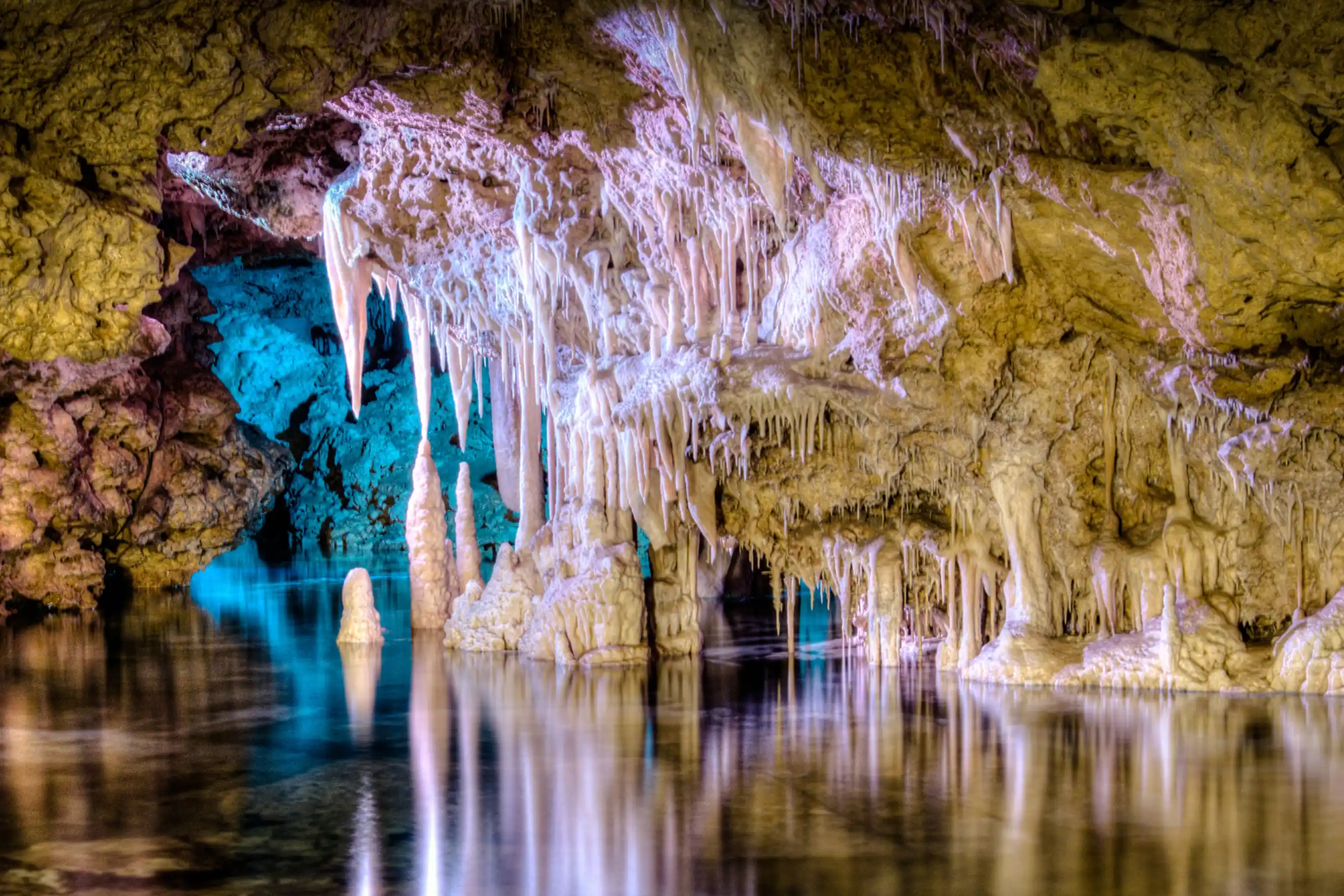 An underground lake reflects lit stalactites and stalagmites inside a large rock cave.