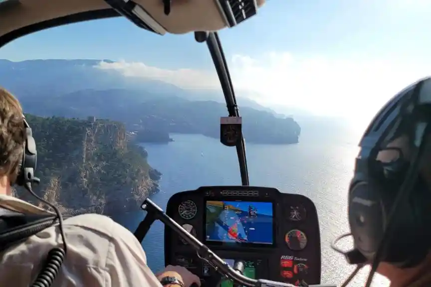View from inside a helicopter cockpit flying over a beautiful coastline with steep cliffs and blue sea.