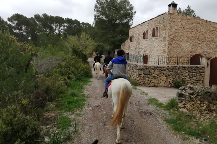 People on a horse riding tour walking along a dirt path next to an old stone country house. People on a horse riding tour walking along a dirt path next to an old stone country house.