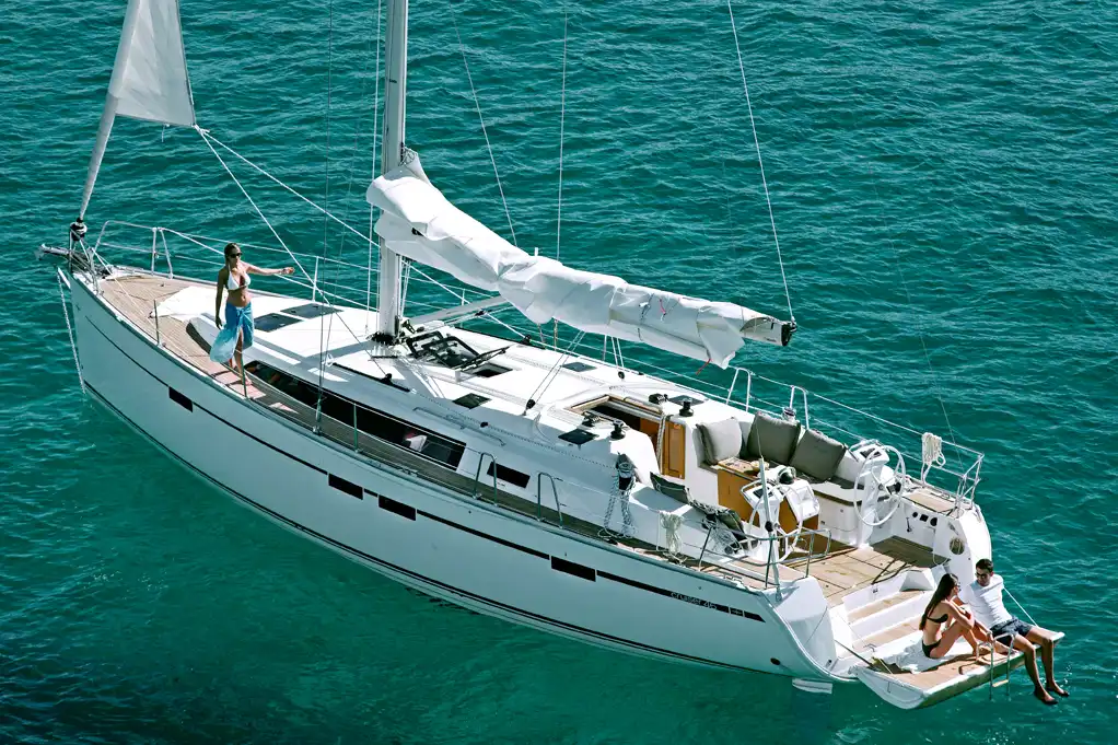 An elevated view of a luxury white sailboat cruising through vibrant turquoise tropical sea water.