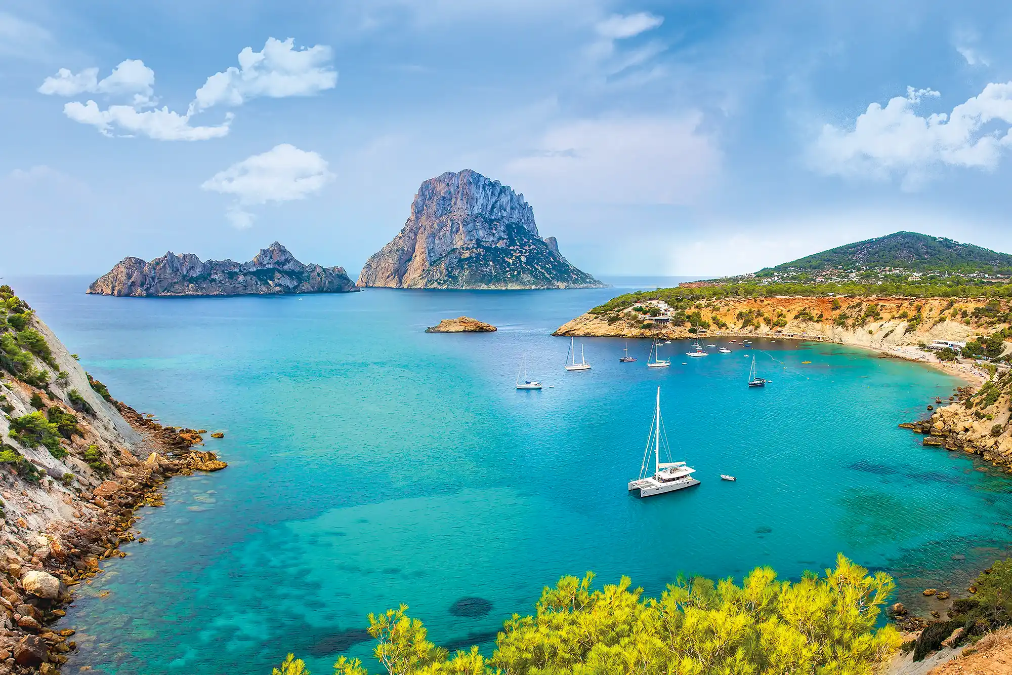 Turquoise bay with anchored sailboats in front of the impressive rocky islet of Es Vedrà.