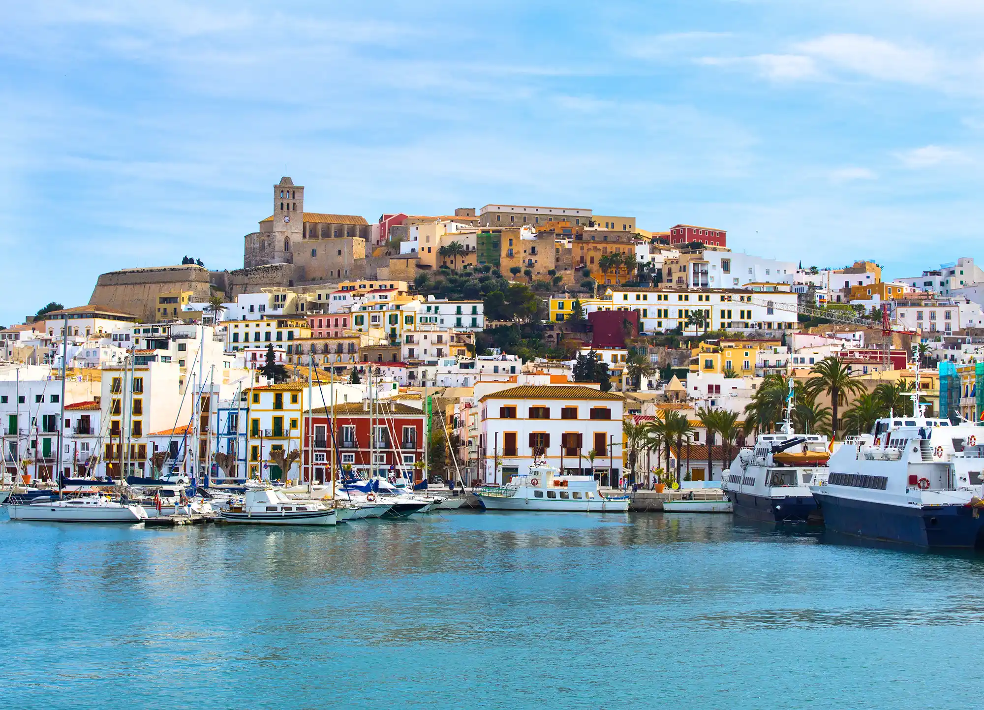 Beautiful view of Ibiza town harbor with historic colorful buildings and boats moored on the water.