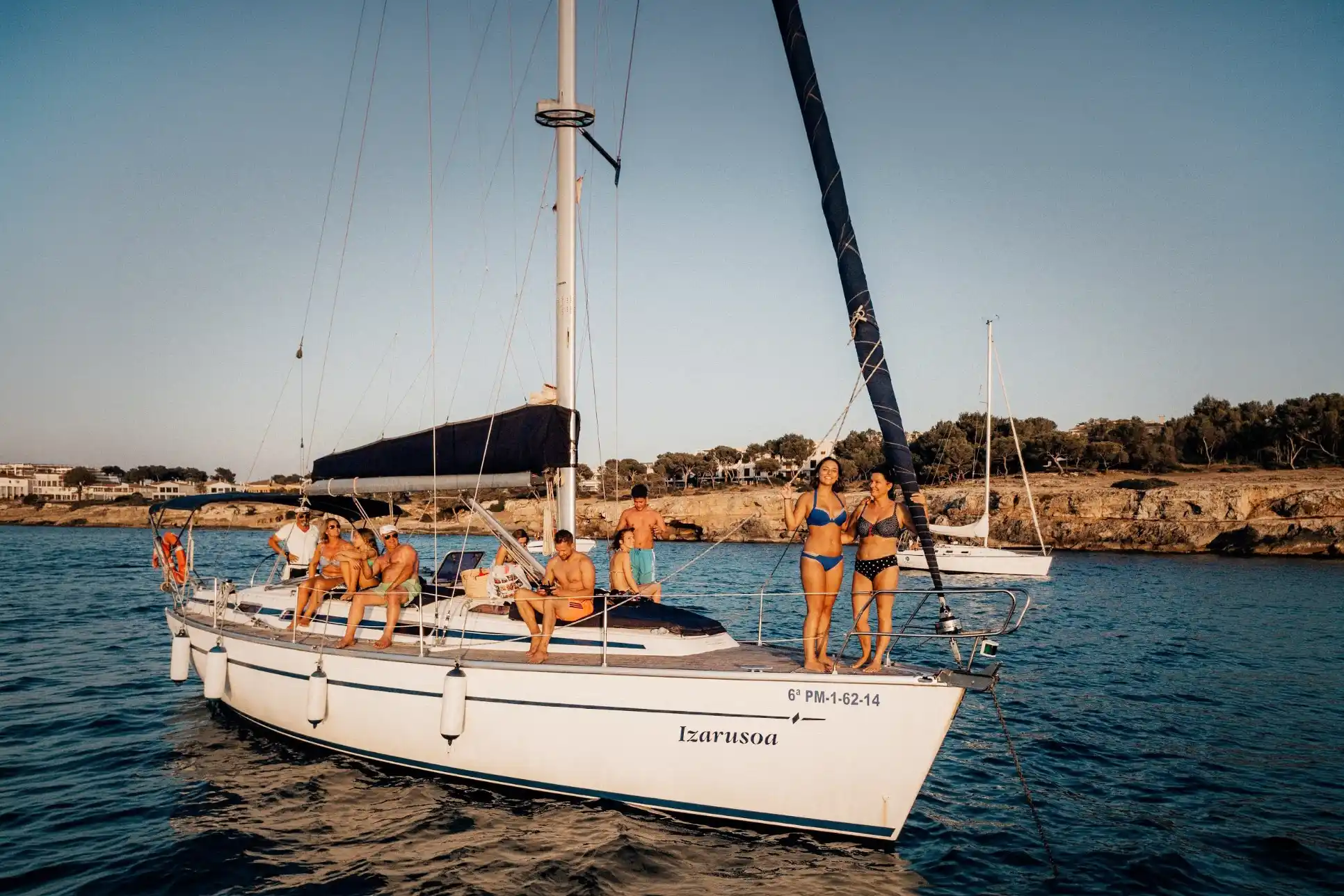 Un grupo de personas disfrutando de una tarde soleada en un velero anclado cerca de una costa rocosa. Un grupo de personas disfrutando de una tarde soleada en un velero anclado cerca de una costa rocosa.