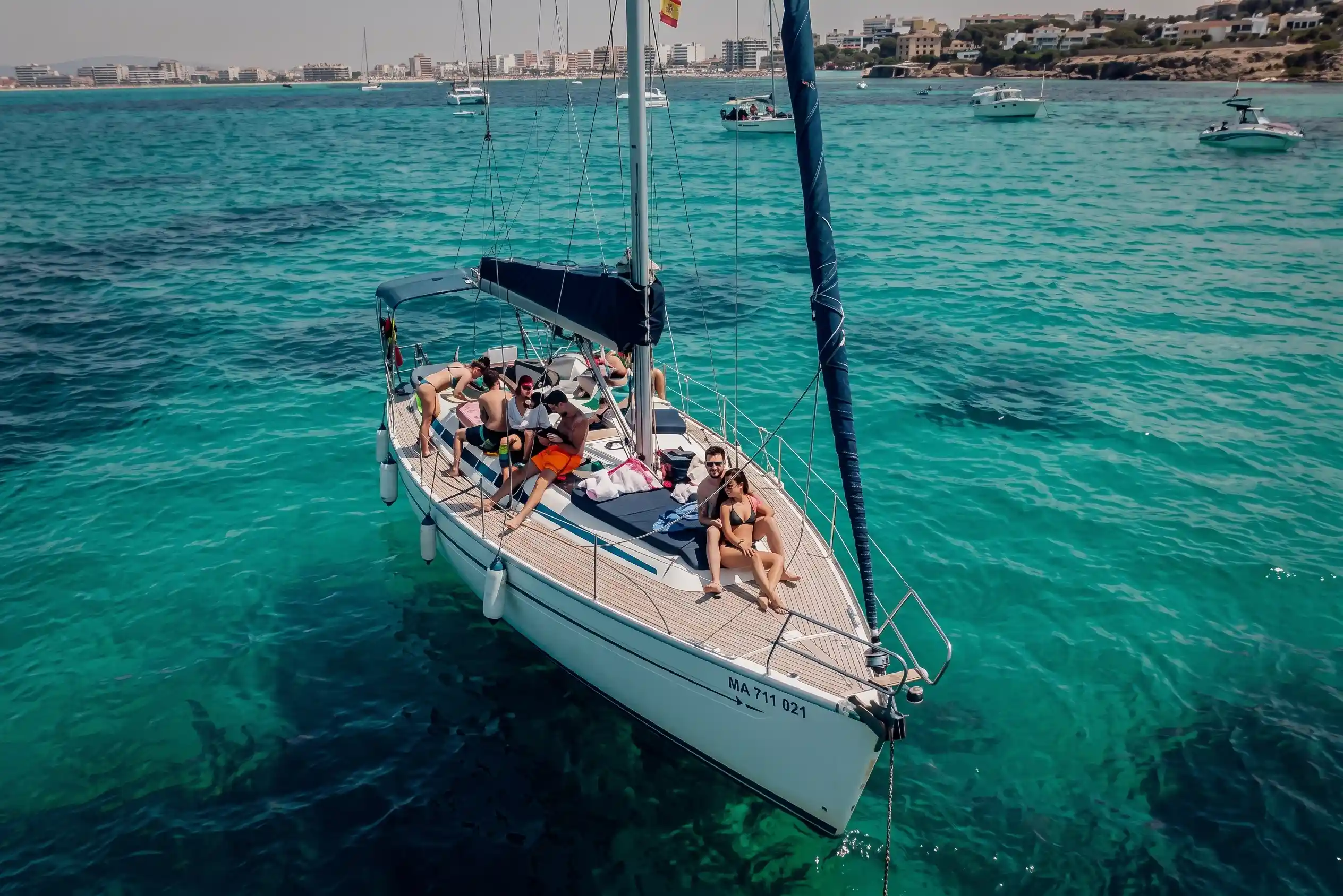 Vista desde lo alto de un velero lleno de gente relajándose en el agua del mar turquesa brillante cerca de la costa.