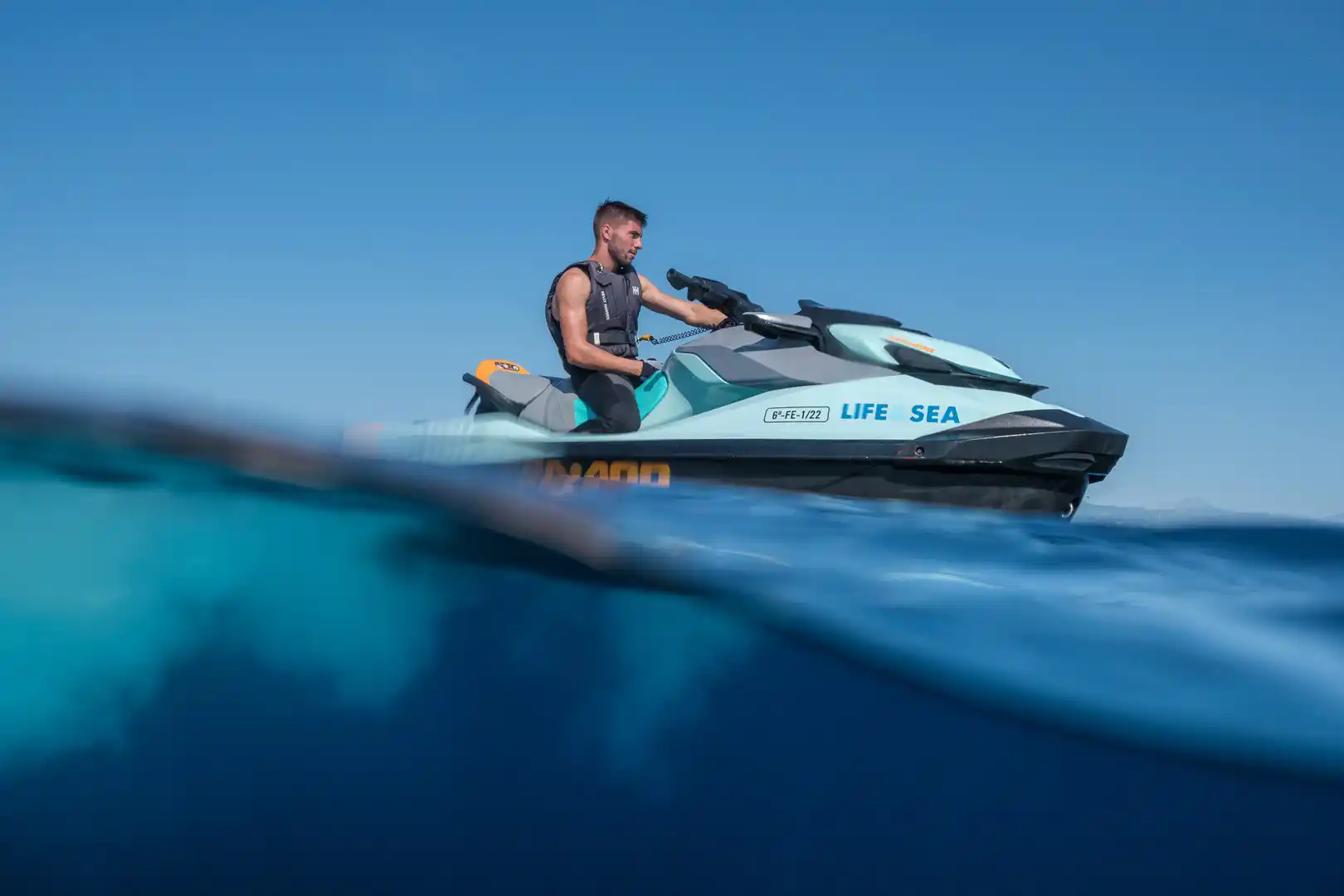 Ein Mann fährt auf einem hellblauen Jetski auf dem Meer mit einer geteilten Unterwasseransicht auf Mallorca.