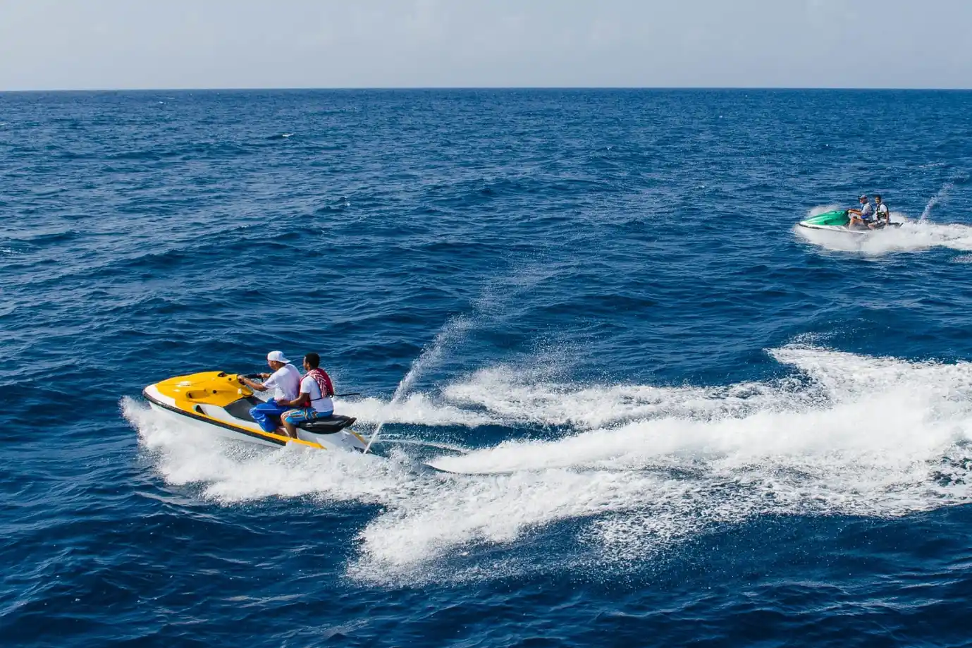 Two people riding a yellow jet ski fast across the deep blue sea creating white waves in Mallorca.