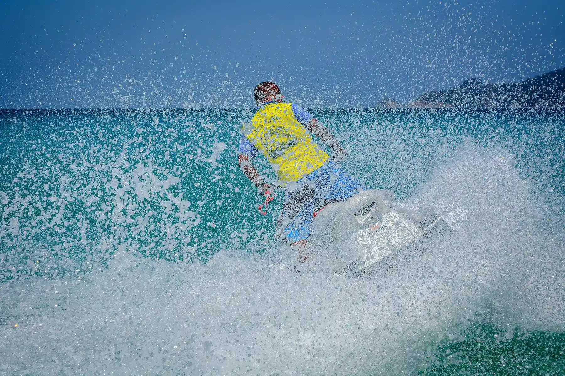 A person on a jet ski speeding through turquoise water, viewed from behind, creating massive white splashes. A person on a jet ski speeding through turquoise water, viewed from behind, creating massive white splashes.