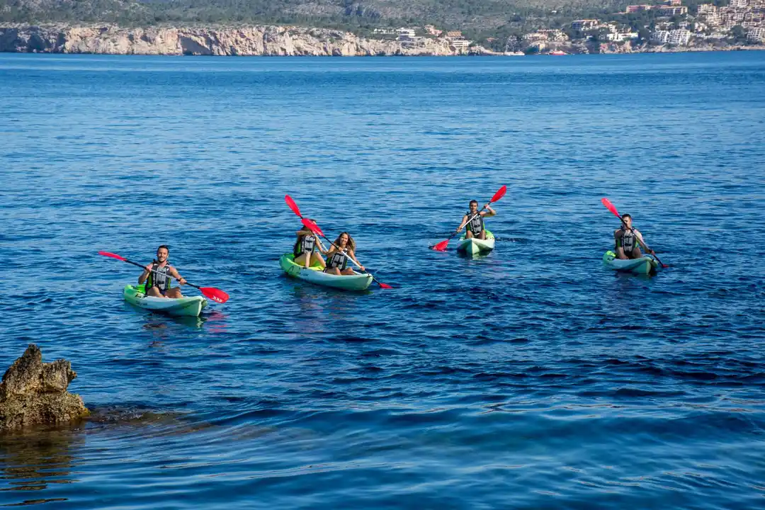 Two people paddle kayaks in the crystal-clear sea water near rocky islets on a bright day.
