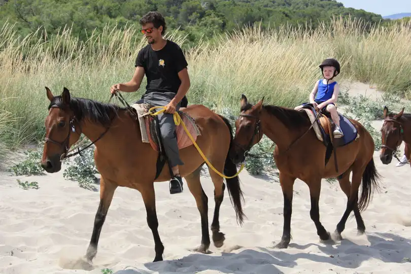 A man and a young child riding horses along a sandy path surrounded by wild grass in Mallorca. A man and a young child riding horses along a sandy path surrounded by wild grass in Mallorca.