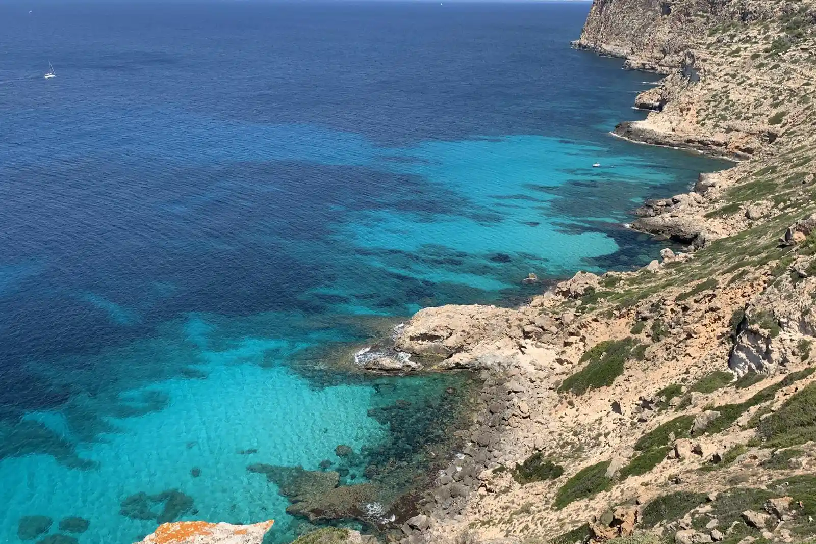 Ein Panoramablick auf kristallklares, türkisfarbenes Wasser an einer felsigen Steilküste unter heller Sonne.