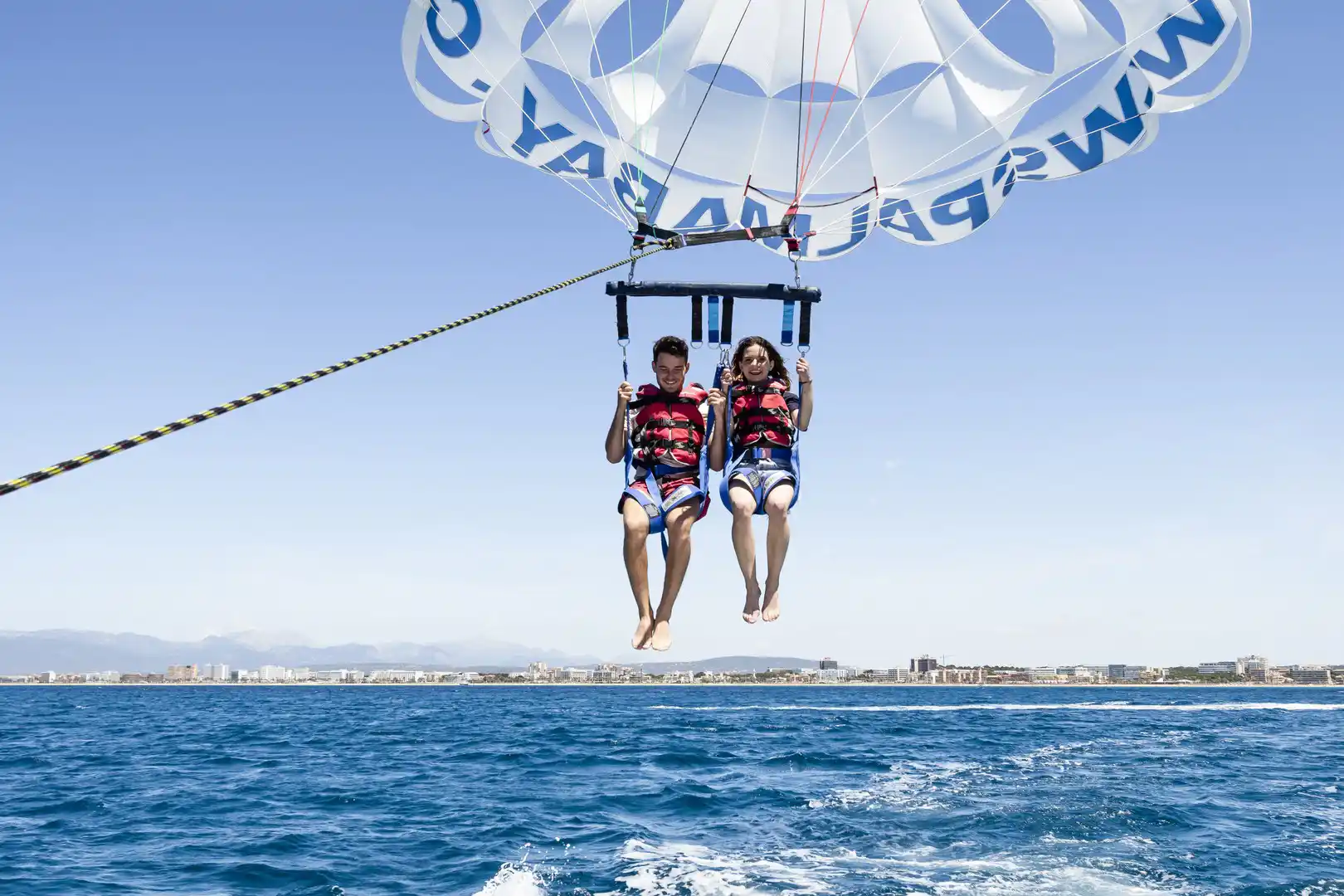 A young couple parasailing high above the blue sea water under a clear sky.