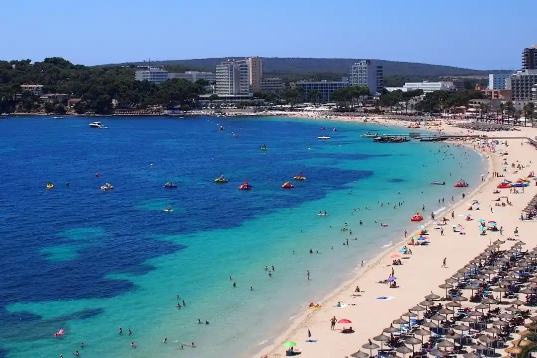 A beautiful curved sandy beach borders vibrant turquoise and blue sea water under a clear sky.
