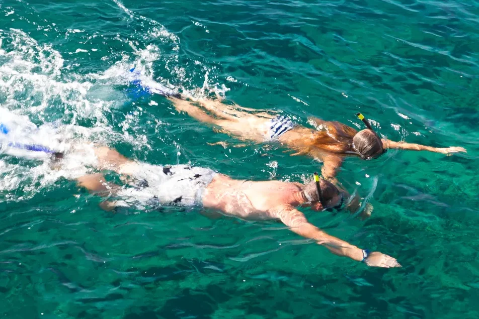 A man and a woman snorkeling side by side in clear turquoise crystal ocean water during summer vacation.