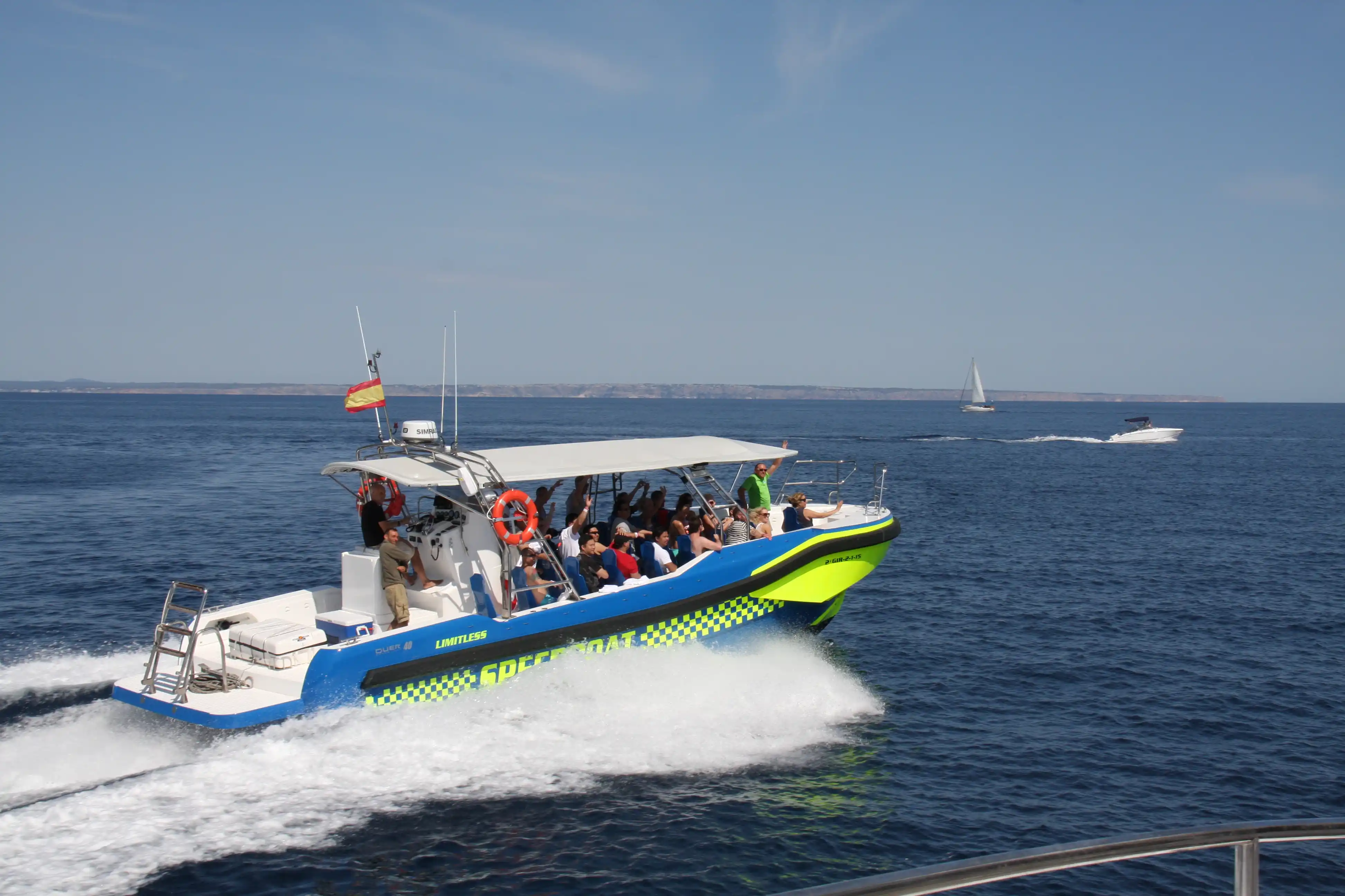 A tourist speedboat filled with passengers cruising fast across the deep blue sea creating white foam.