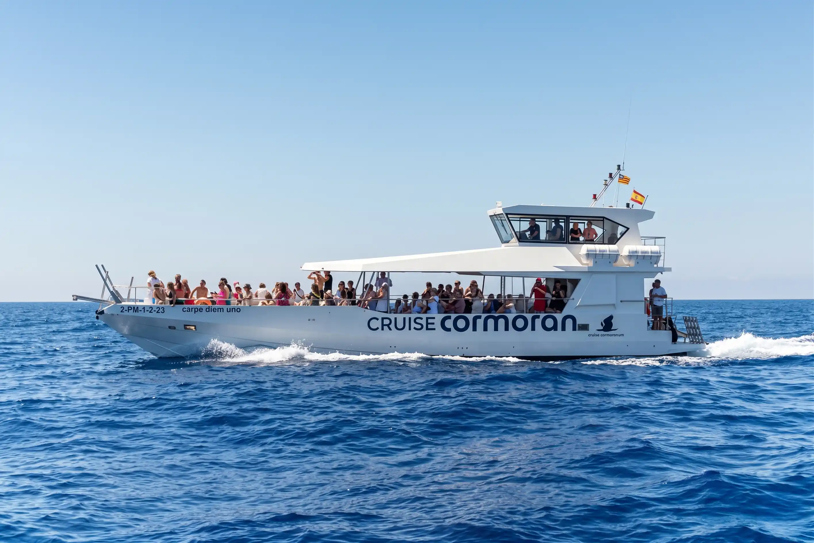 English: Large cruise boat "Cruises Cormoran" filled with passengers sailing on the blue sea water under a clear sky.