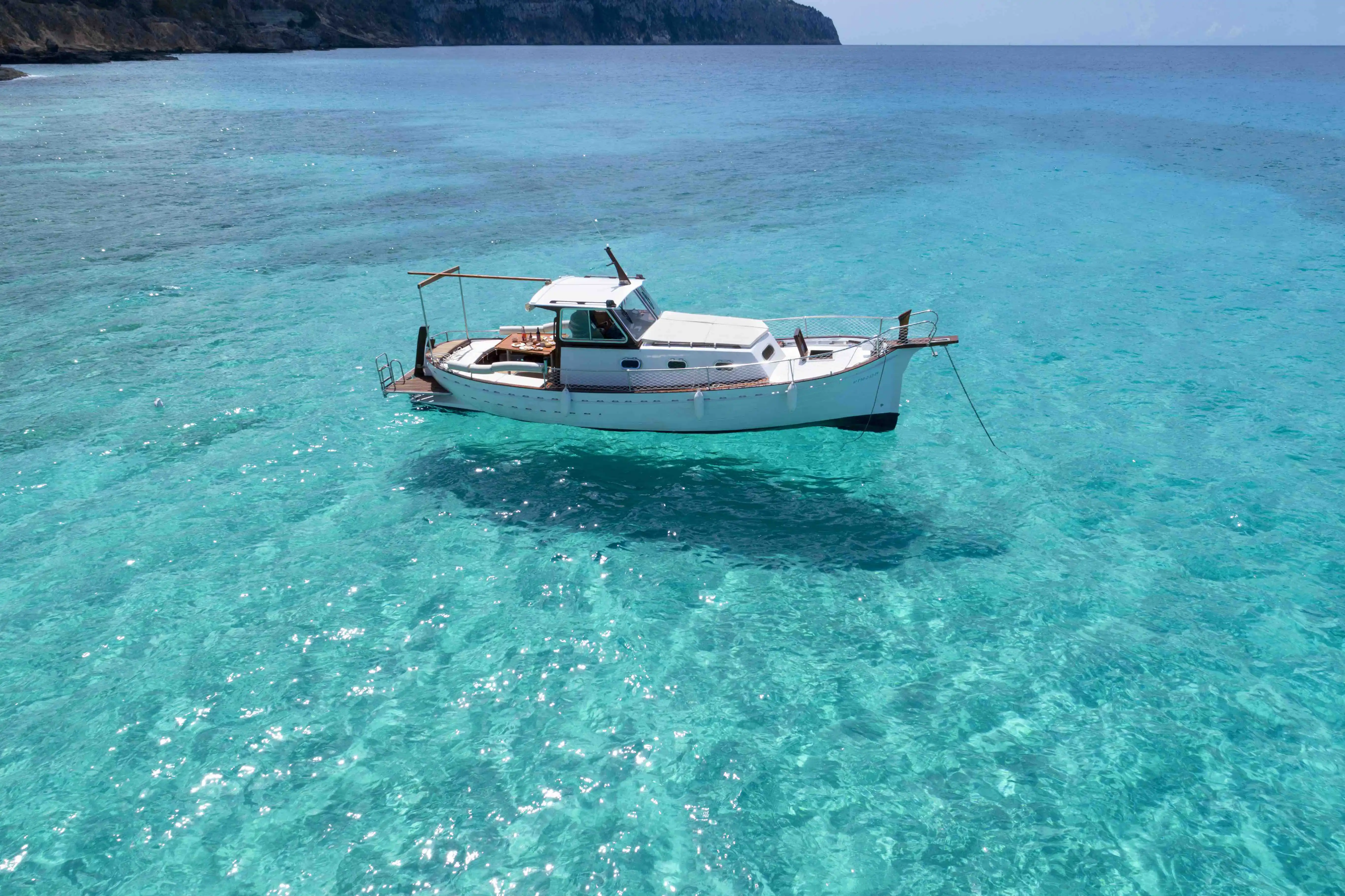 Luftaufnahme eines weißen Bootes, das seinen Schatten auf das klare, türkisfarbene Meer auf Mallorca wirft. Luftaufnahme eines weißen Bootes, das seinen Schatten auf das klare, türkisfarbene Meer auf Mallorca wirft.