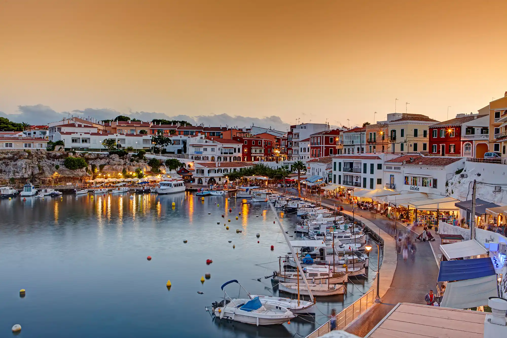 Beautiful harbor town illuminated at sunset with numerous boats moored along the calm waterfront.