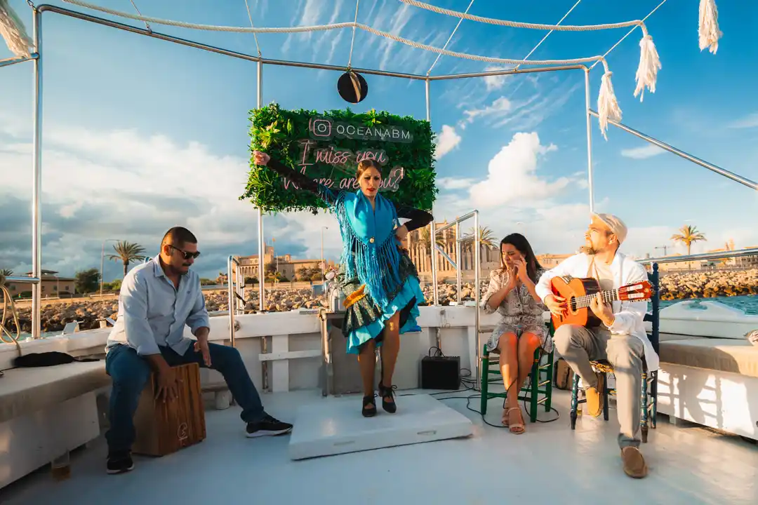 A flamenco dancer performs on a boat deck accompanied by musicians under a partly cloudy sky.